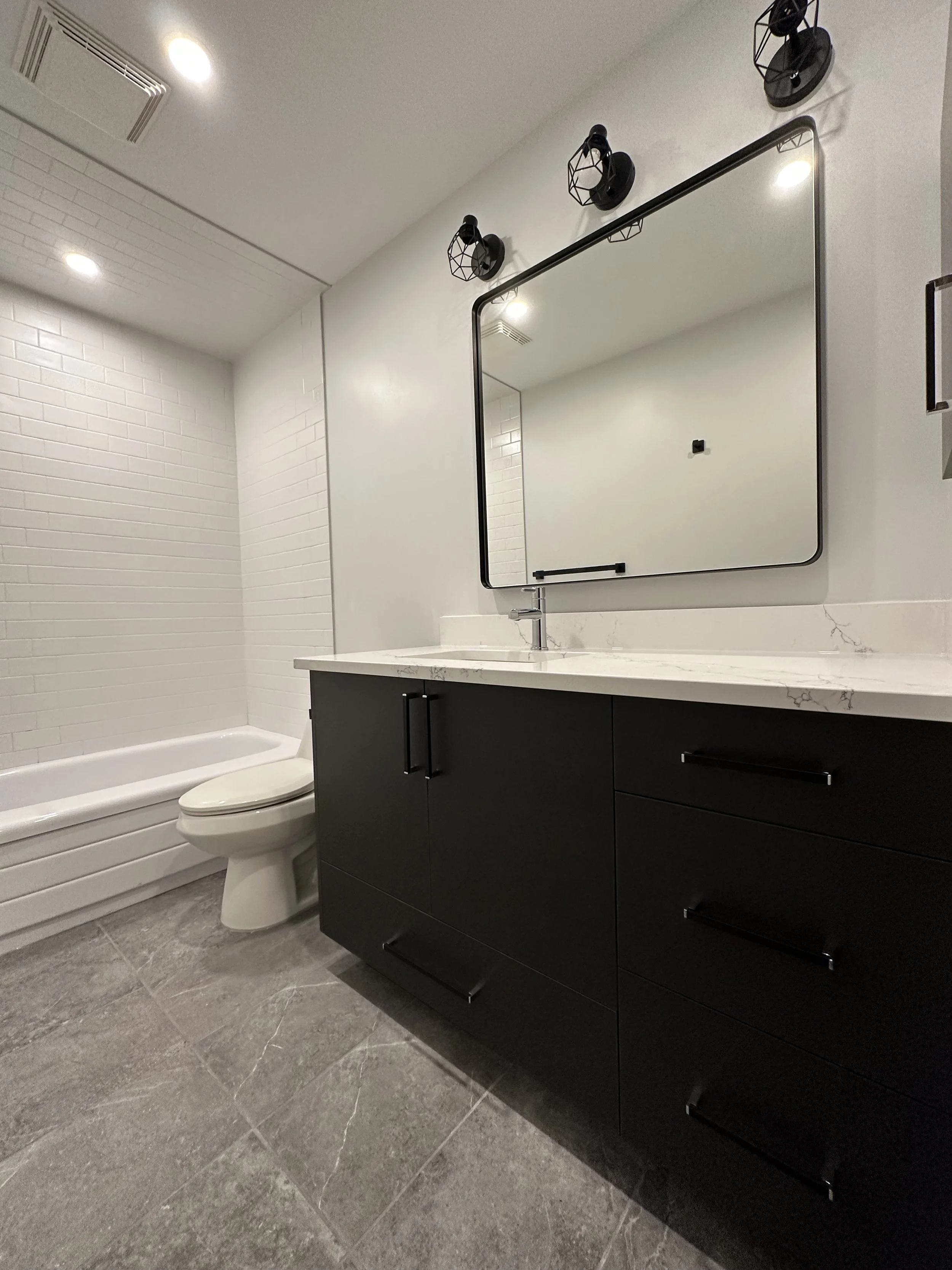 Calgary Renovation Contractor contemporary bathroom with black vanity, quartz countertop, subway tile tub surround, and modern lighting.