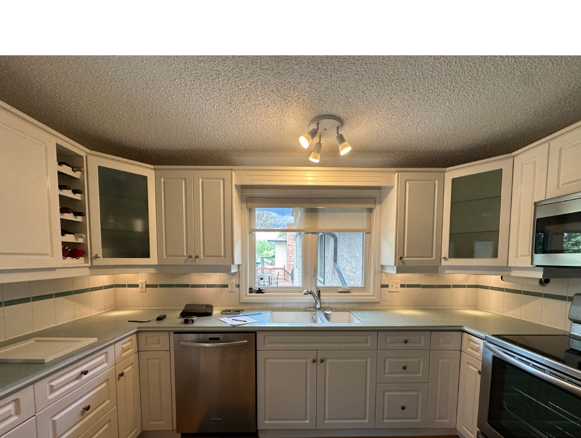 Calgary kitchen before renovation with white raised-panel cabinets, laminate countertops, and fluorescent lighting