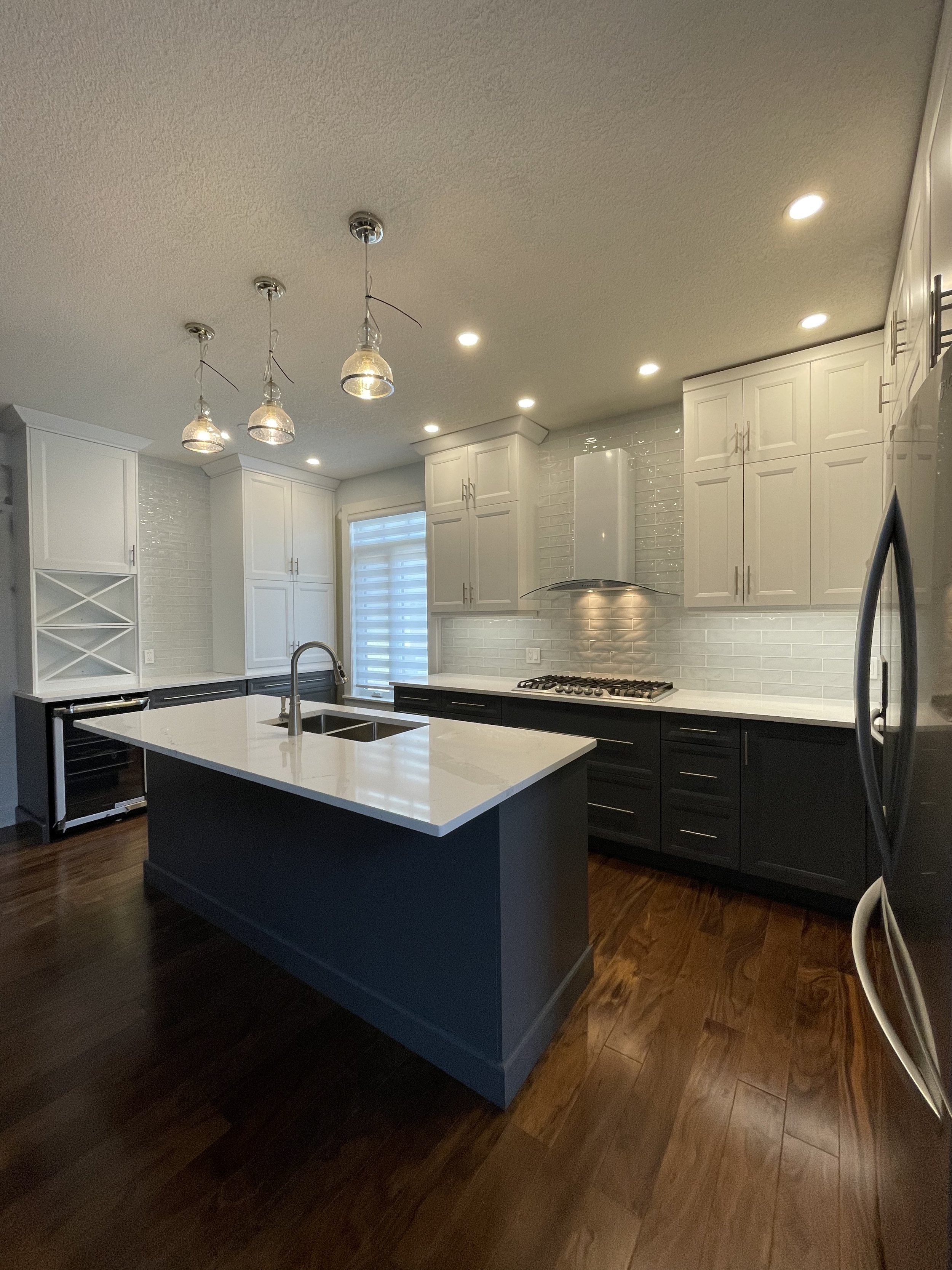 Modern Calgary kitchen renovation after with white upper cabinets, navy island, quartz countertops, and pendant lighting.