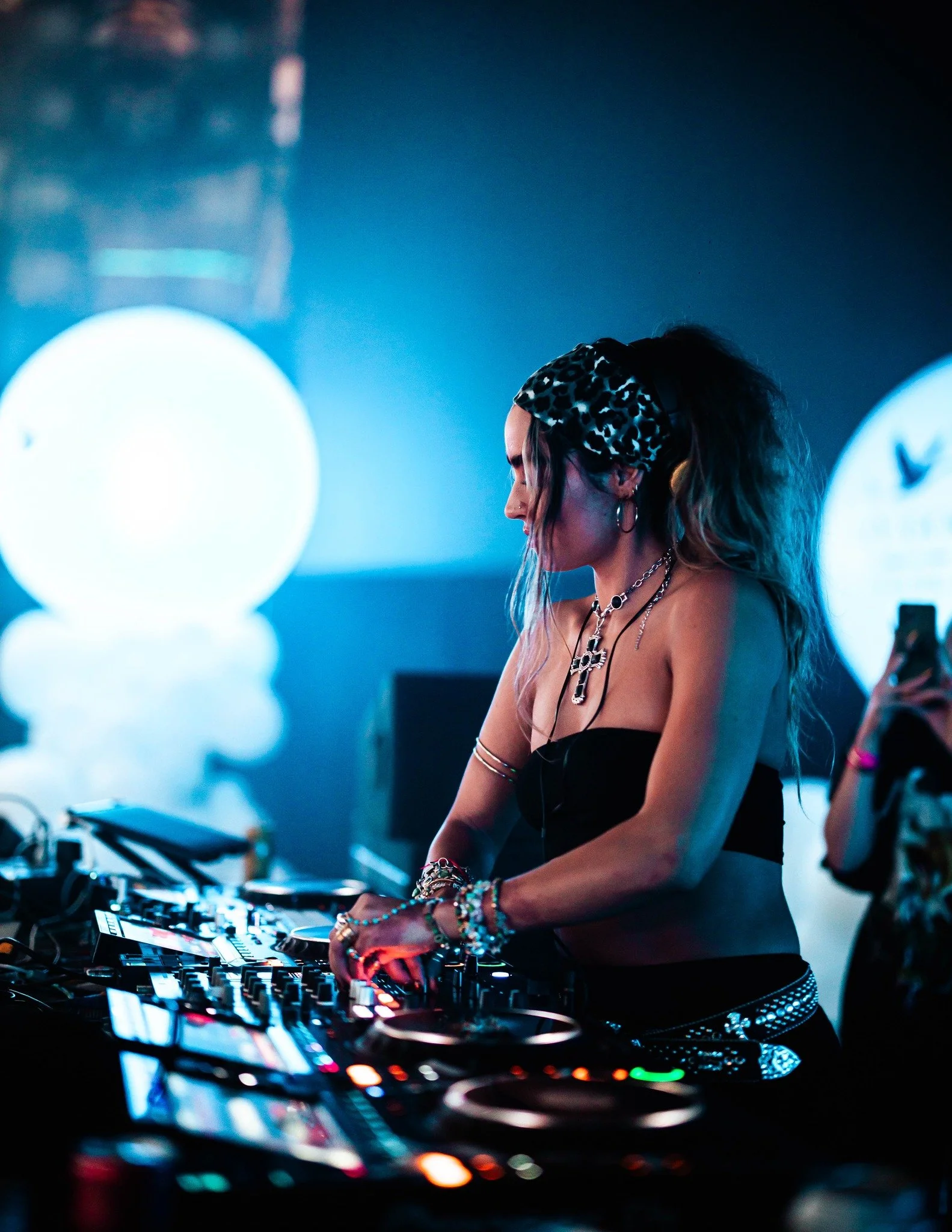 DJ wearing a leopard-print headband mixing music on a DJ controller at a blue-lit nightclub