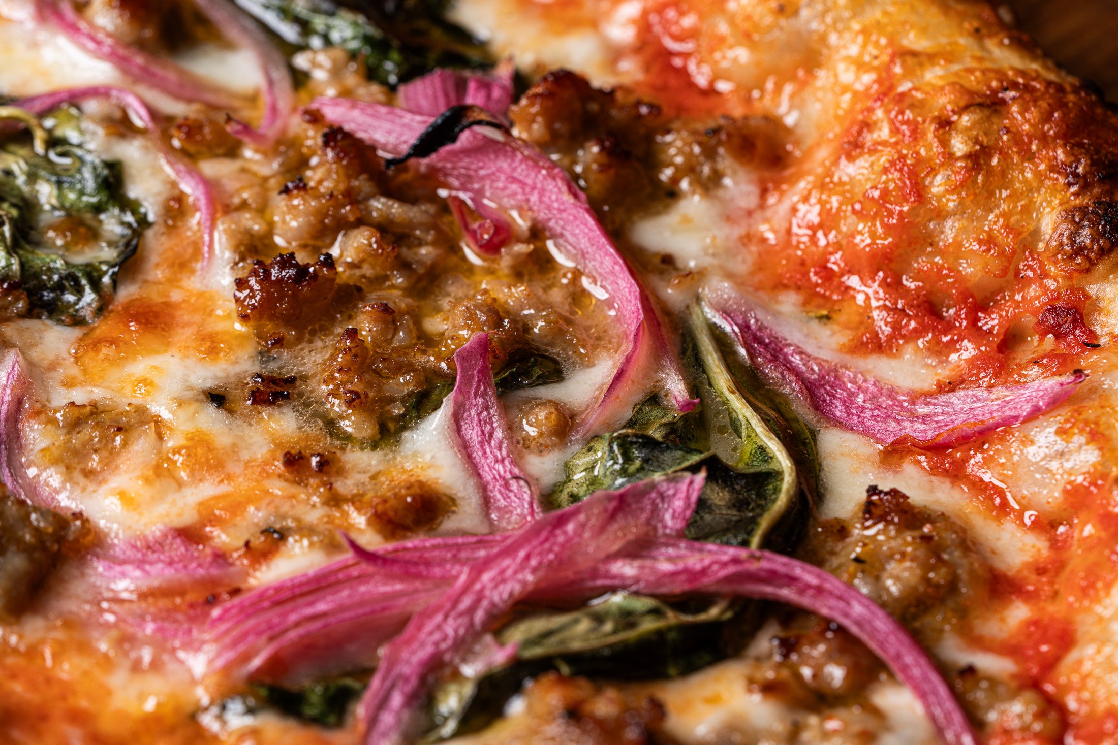 vibrant pickled red onions with fresh basil and Italian sausage perfectly baked into mozzarella cheese on naturally leavened sourdough crust