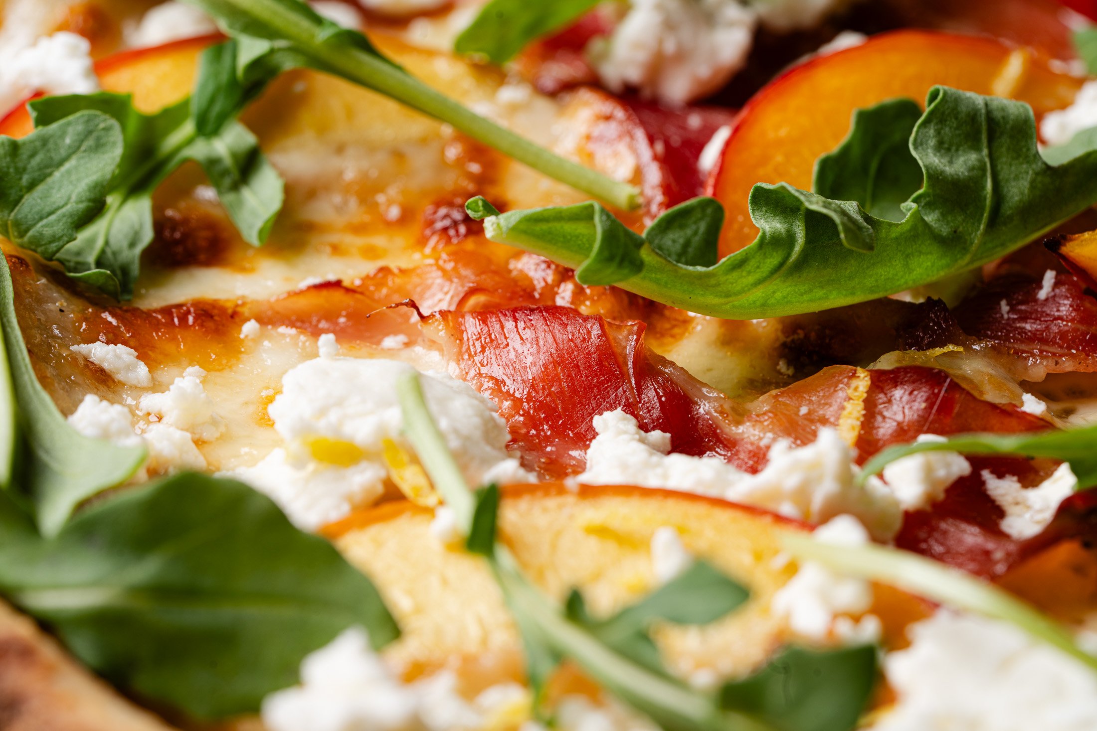 A close up view of peaches, cheese, prosciutto, and arugula on the Genevieve special.
