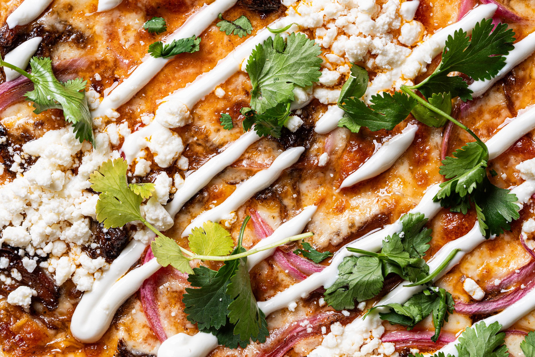 close up view of the birria, queso fresco, pickled red onion, cilantro and Mexican crema on the LA Taco pizza