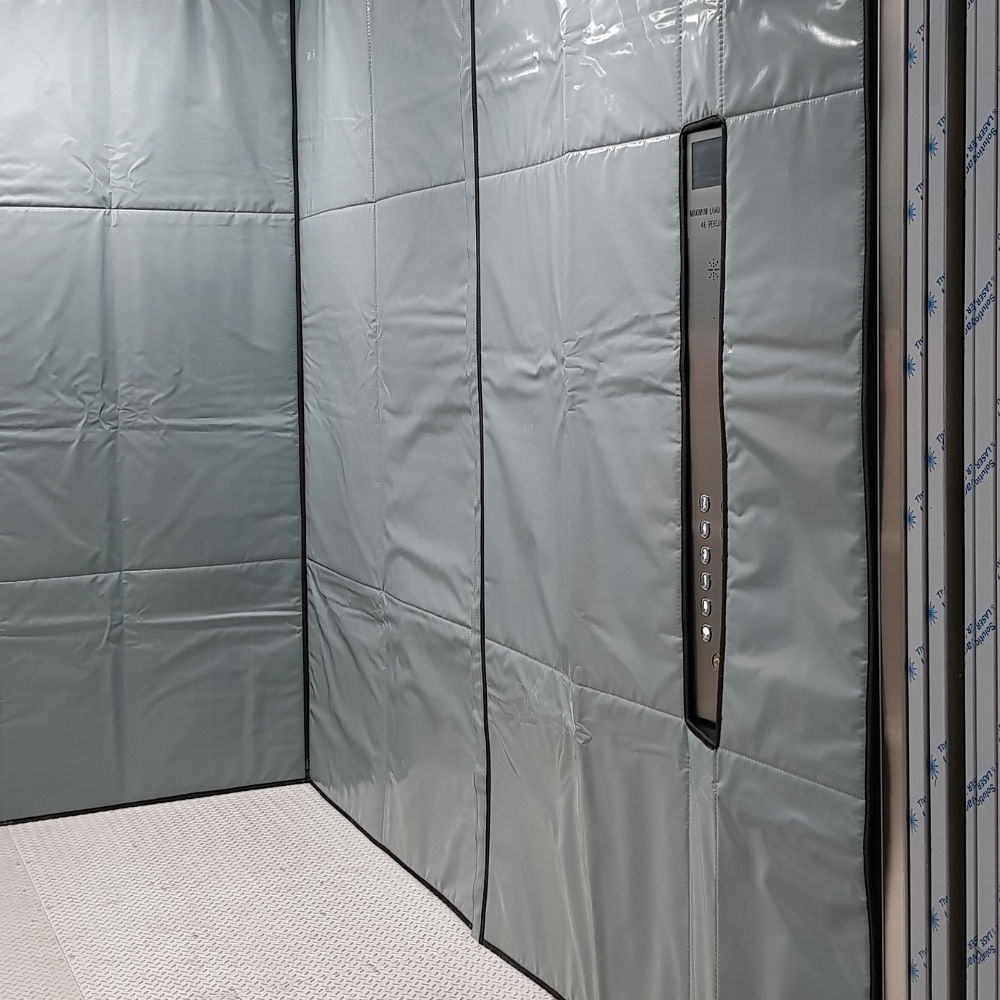 Elevator interior with padded silver walls and a control panel with multiple buttons.