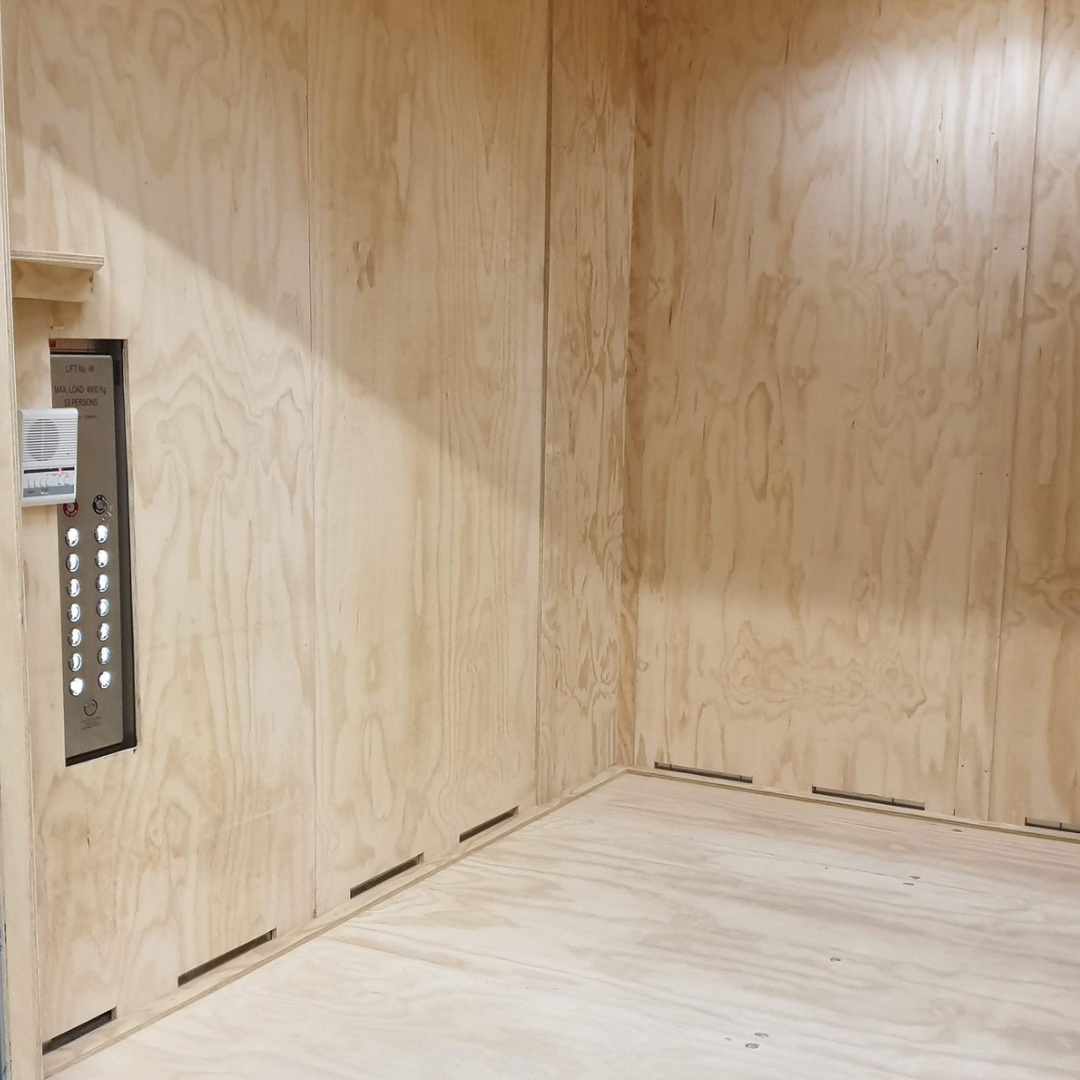 Empty elevator interior with wood panel walls and floor, elevator control panel with floor buttons on the left wall.