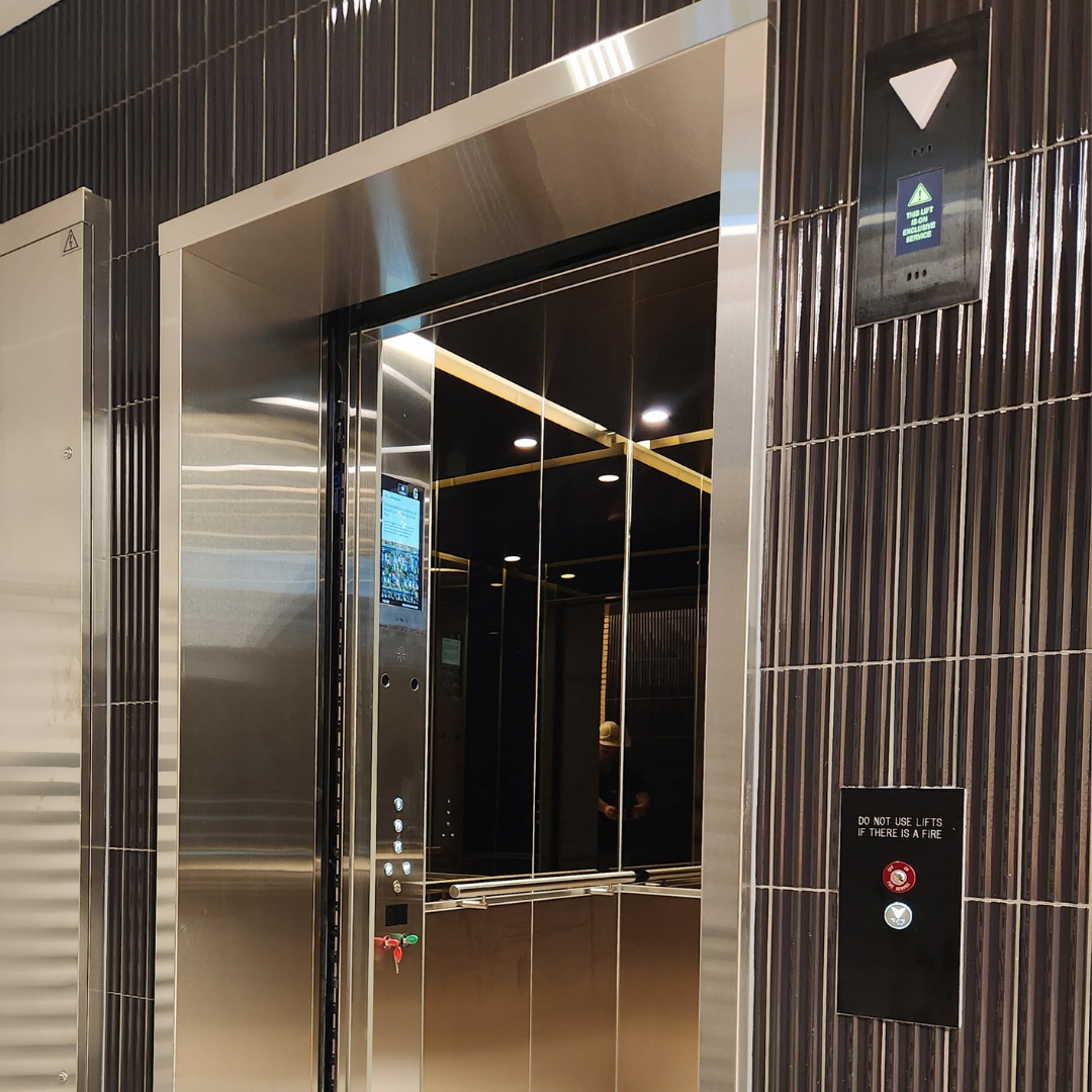 Modern elevator with mirror interior, digital display on the control panel, and black tiled walls with gold accents.