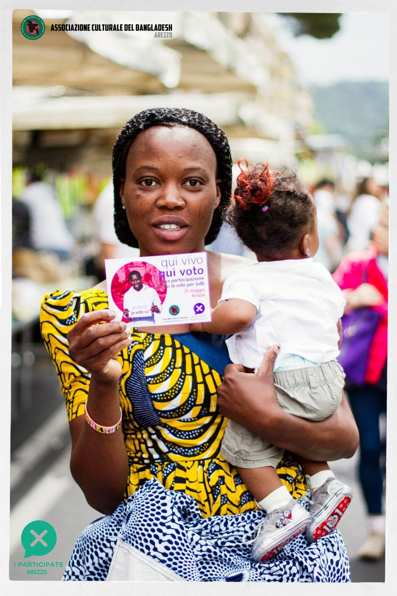 Una donna con un bambino mostra una cartolina della campagna I PARTICIPATE.