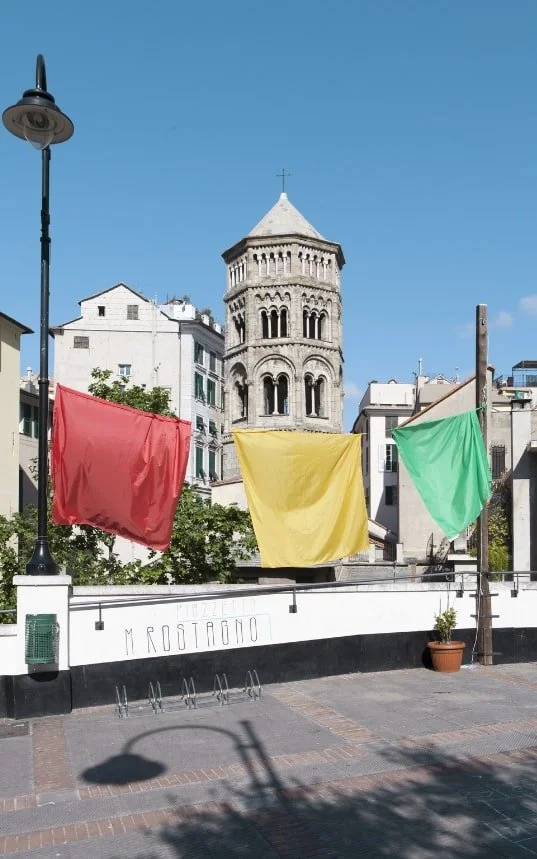 Teli colorati in uno spazio all’aperto con una torre sullo sfondo, per il progetto MERAVIGLIA.