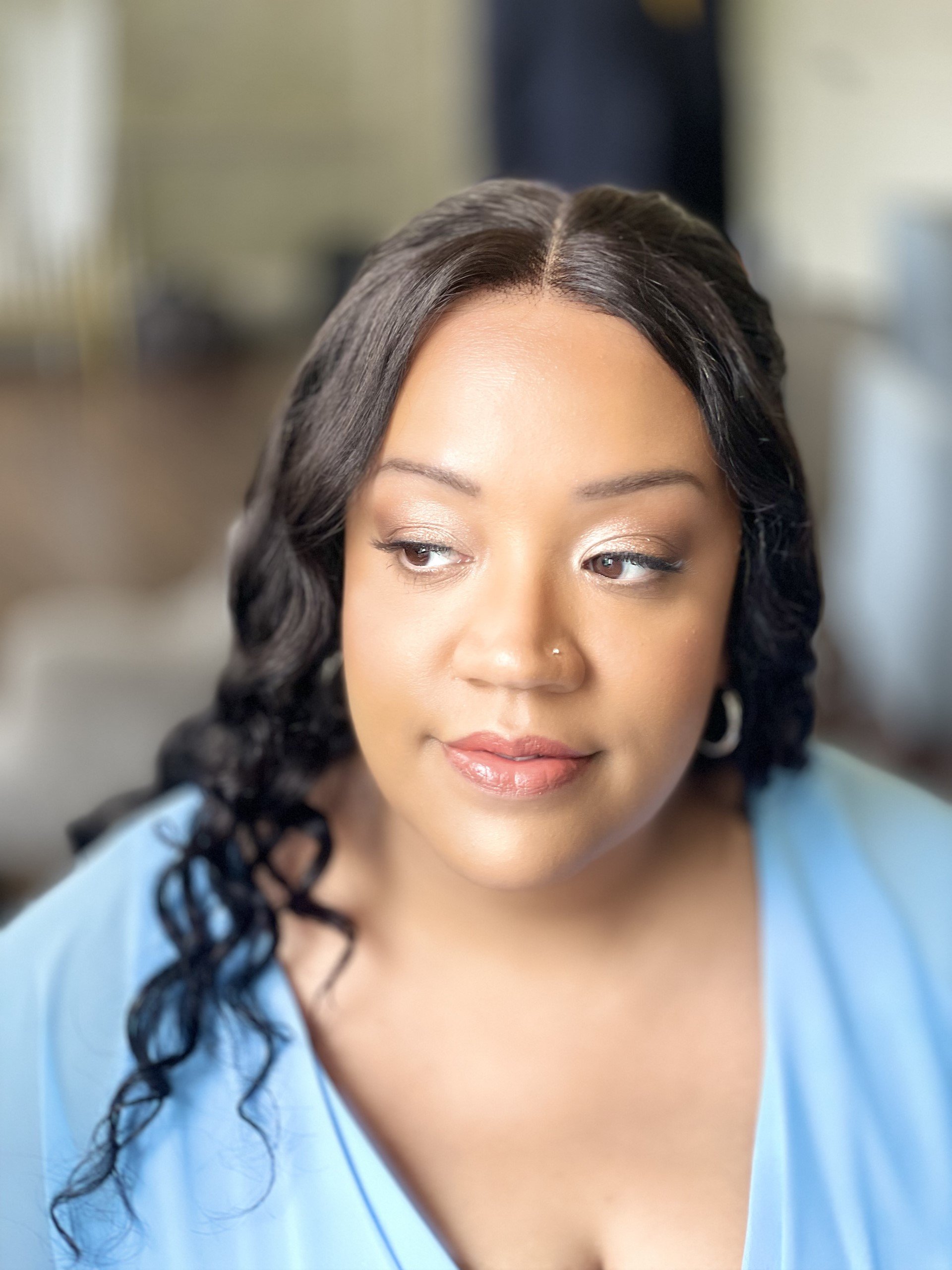 Close-up portrait of a woman with dark, curly hair wearing a light blue top, looking to the side with a soft expression.