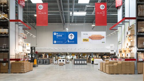 Empty aisle in a home improvement store with red and white signage overhead.