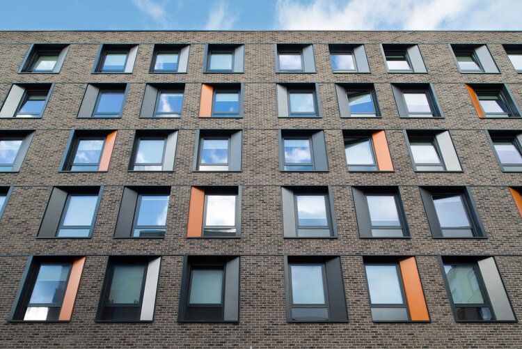 Apartment building with brick facade and multiple windows reflecting the sky.