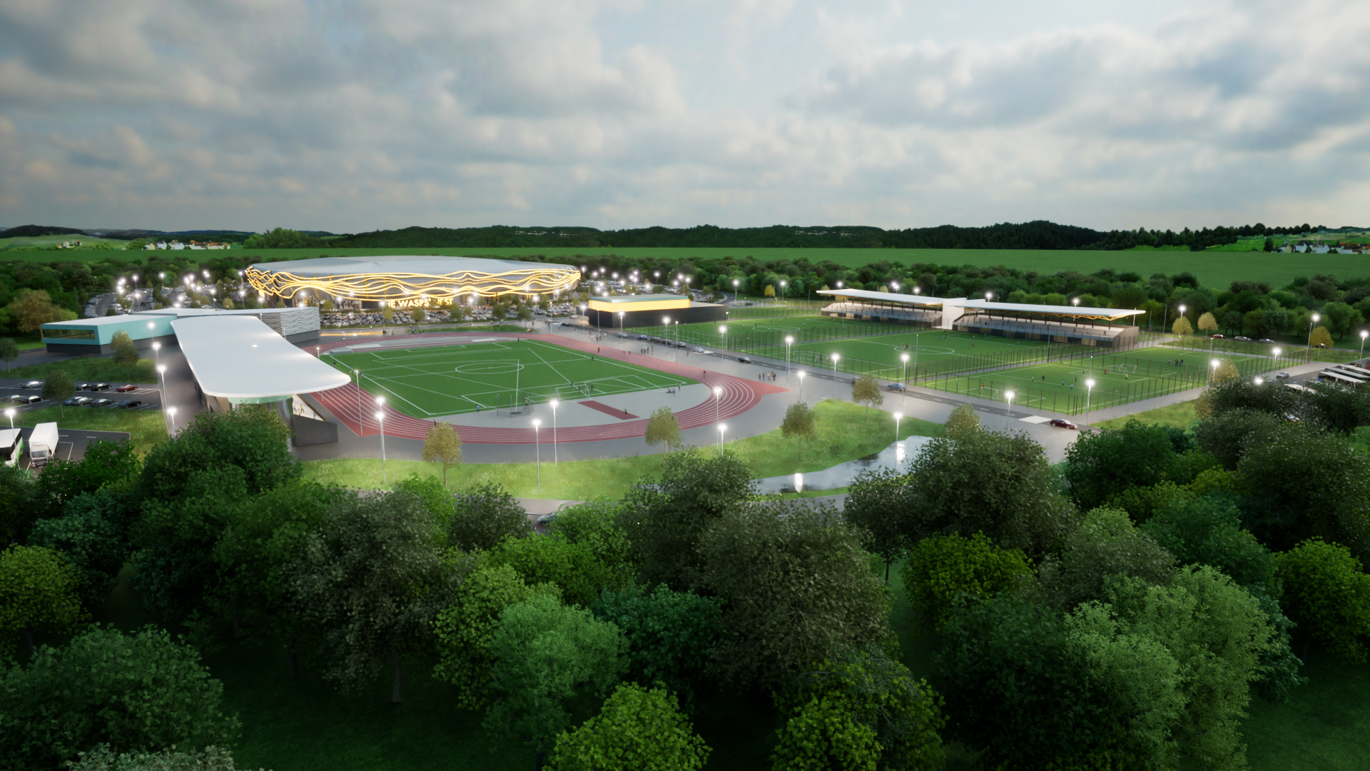 A bird's-eye view of a modern sports complex at dusk, featuring multiple soccer fields, a running track, parking lots, and surrounding trees, with city lights beginning to turn on.