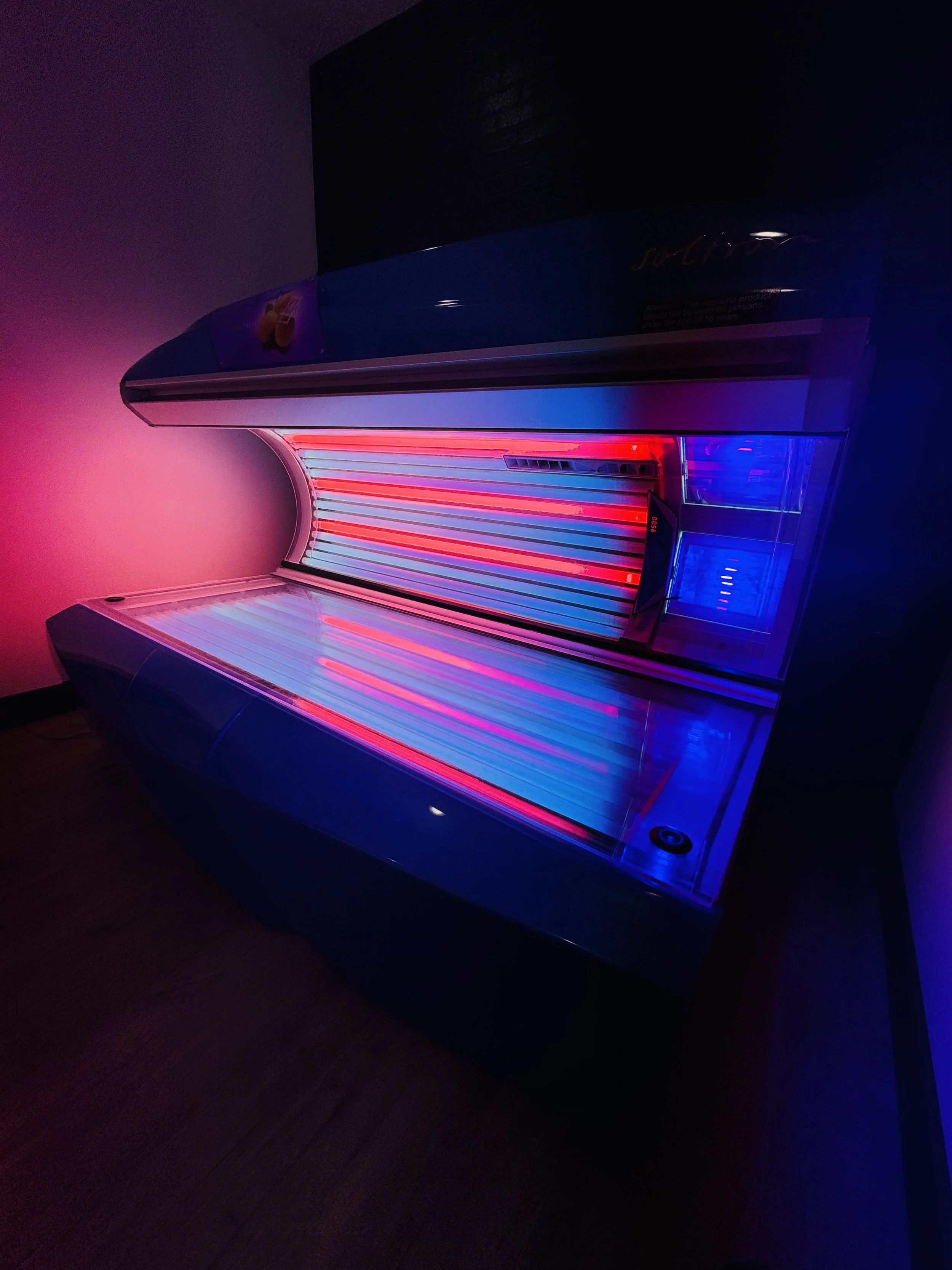 A tanning bed with glowing red and blue lights in a dimly lit room.