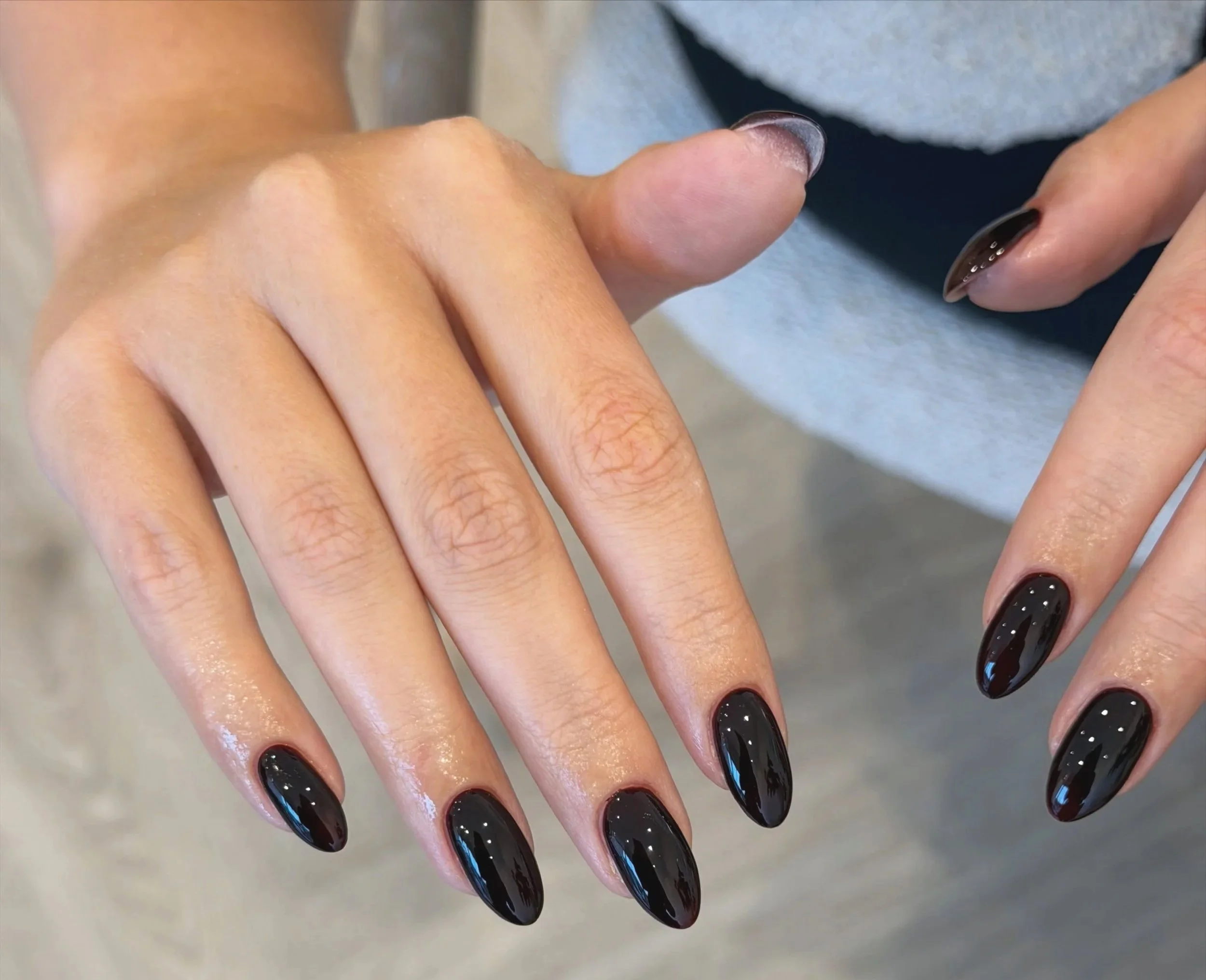 Close-up of a person's hand with nails painted with black gel polish with white dots, resting on a light surface.