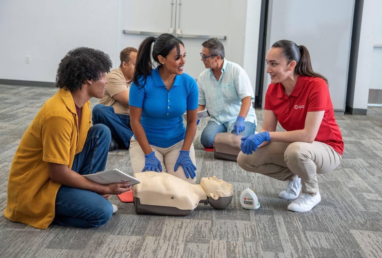 Group of people practicing CPR on mannequins during a training session in a classroom.