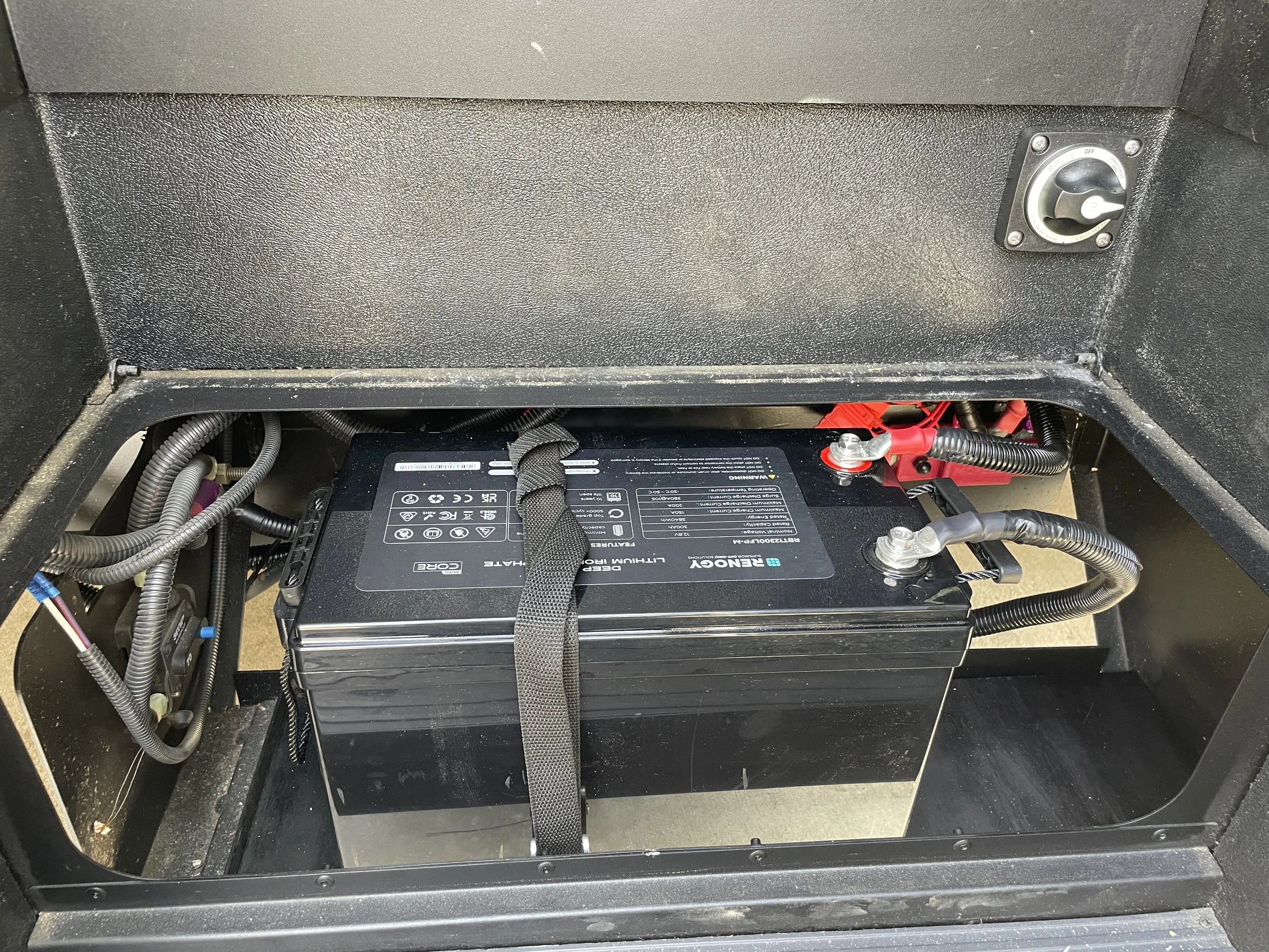 A black battery with labels and cables under step Example of RV Solar Install near San Diego.  Lithium Battery, DC/DC Converter, LiFePO4, Inverter, install on RV near San Diego, CA.