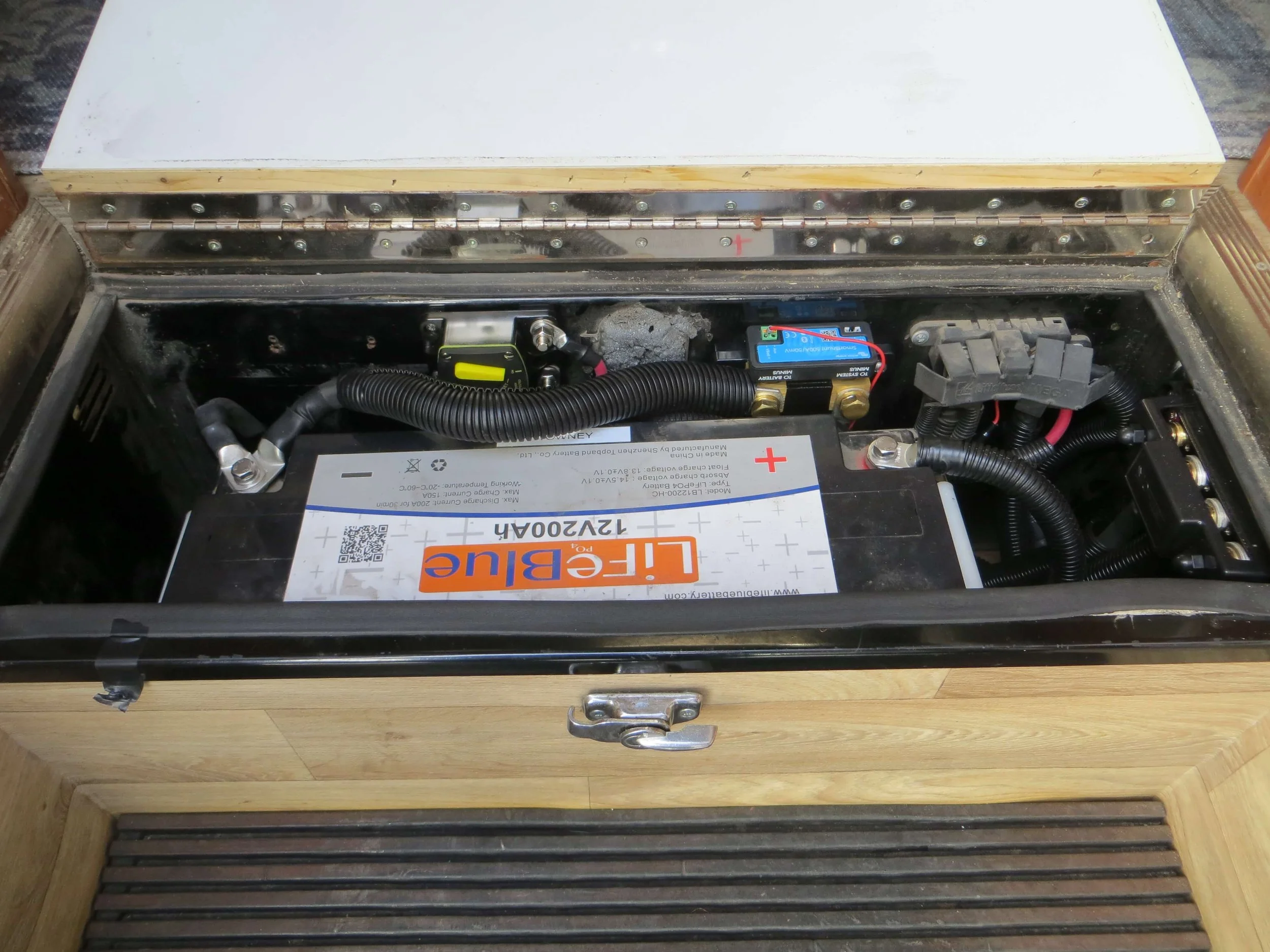 Inside a wooden compartment, a large car battery labeled 'Life Blue' Example of RV Solar Install near San Diego.  Lithium Battery, DC/DC Converter, LiFePO4, Inverter, install on RV near San Diego, CA.