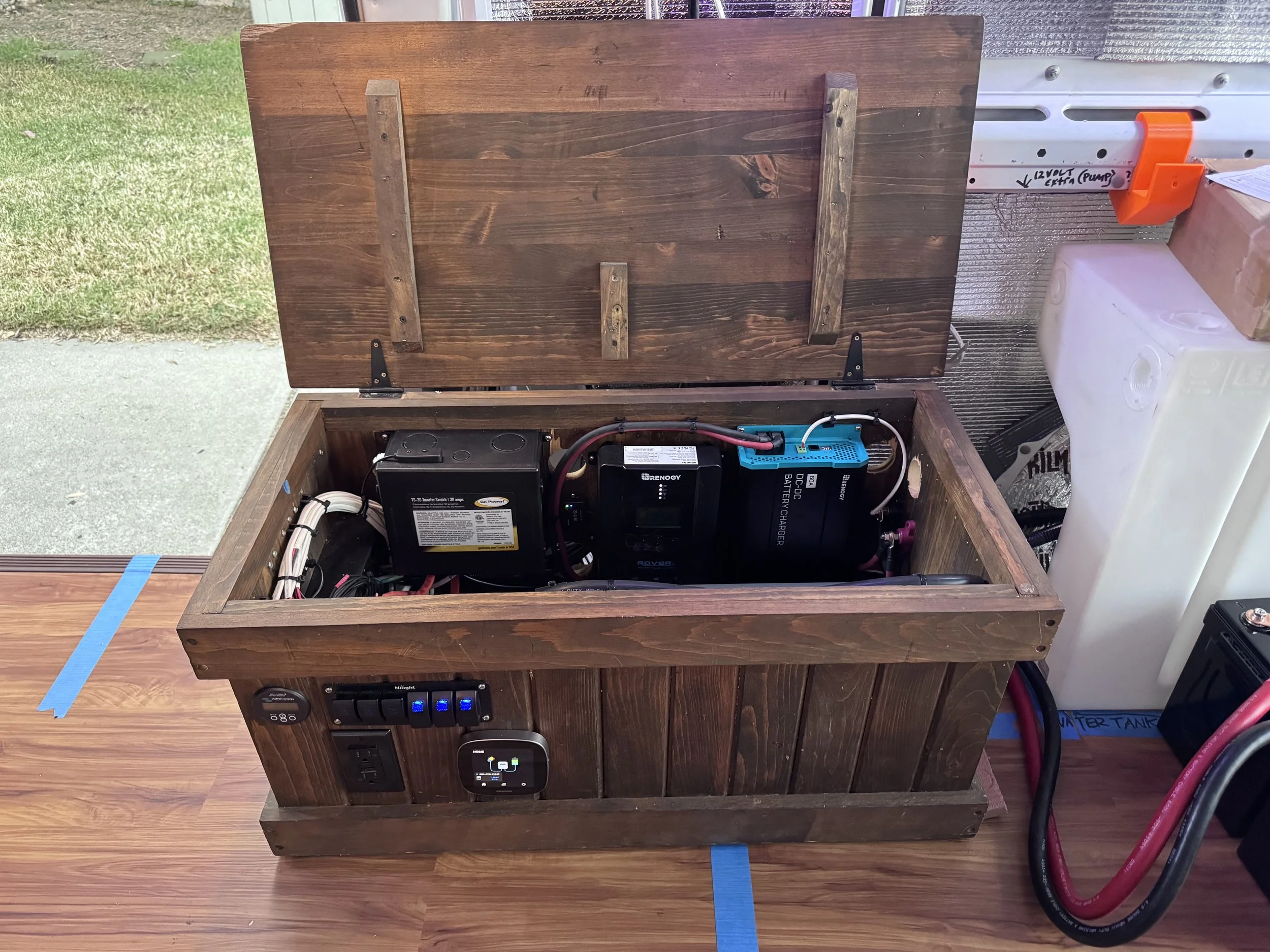 A wooden outdoor storage box containing an electrical battery and charger setup for a solar power system. Example of RV Solar Install near San Diego.  Lithium Battery, DC/DC Converter, LiFePO4, Inverter, install on RV near San Diego, CA.