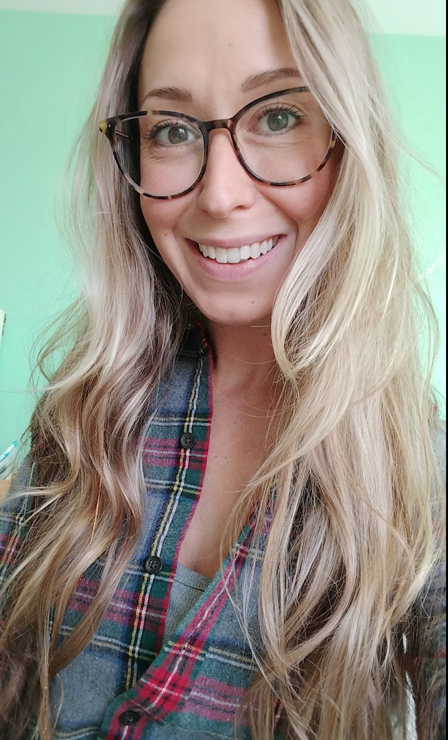 A woman with long, wavy blonde hair, wearing glasses and a plaid shirt, smiling at the camera.