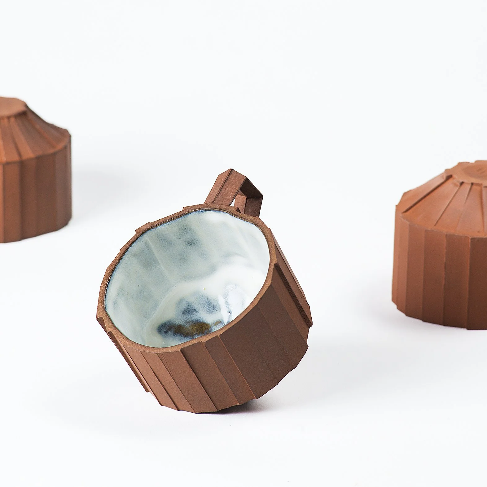 Handmade faceted ceramic cup with unglazed red stoneware exterior and off-white glazed interior, by Lea Nicolas
