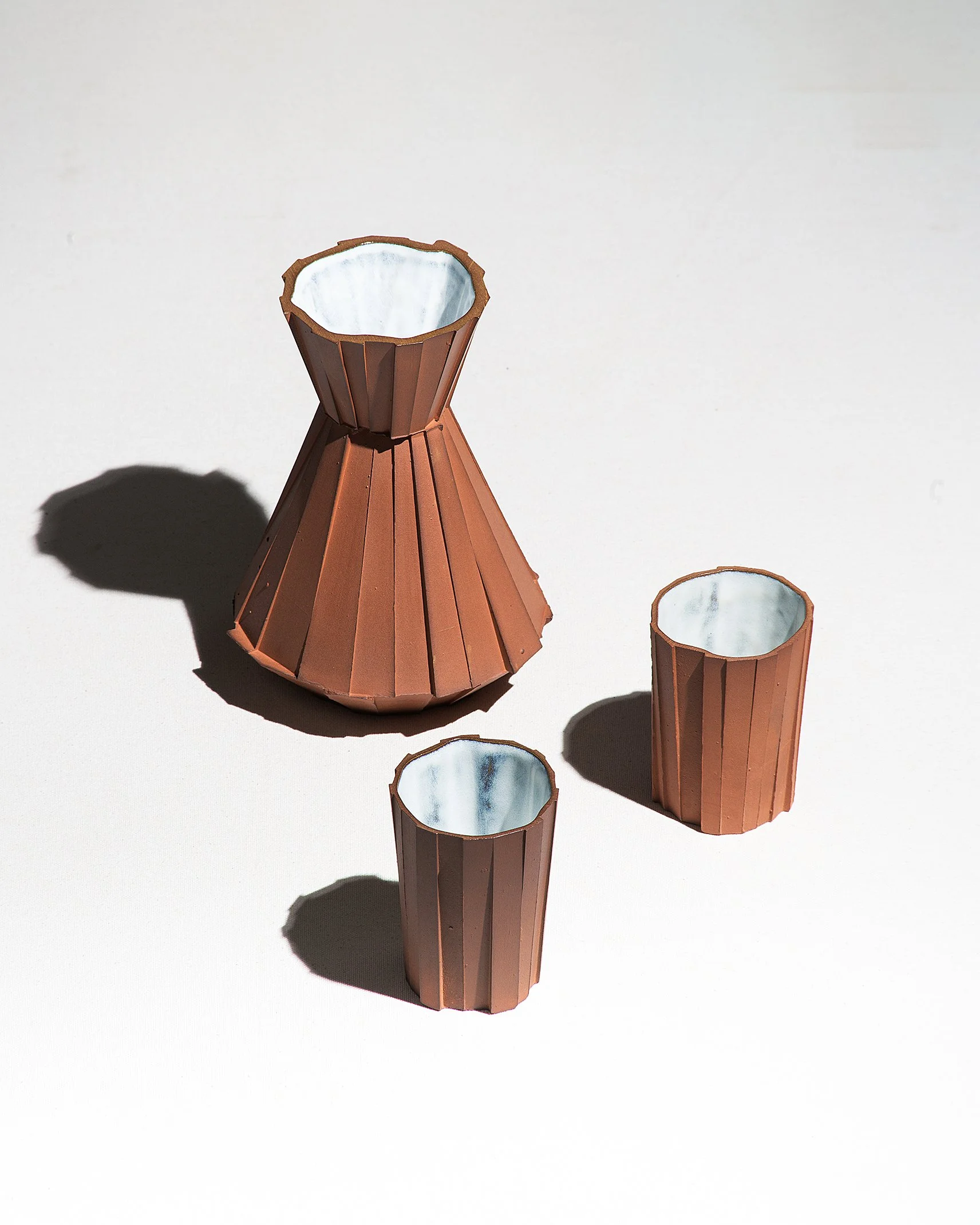 Handmade faceted ceramic carafe with unglazed red stoneware exterior and off-white glazed interior, by Lea & Nicolas