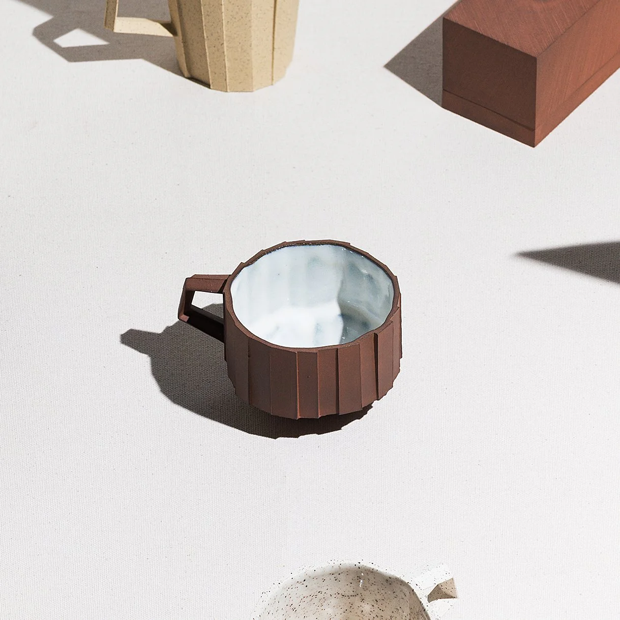 Handmade faceted ceramic cup with unglazed red stoneware exterior and off-white glazed interior, by Lea Nicolas