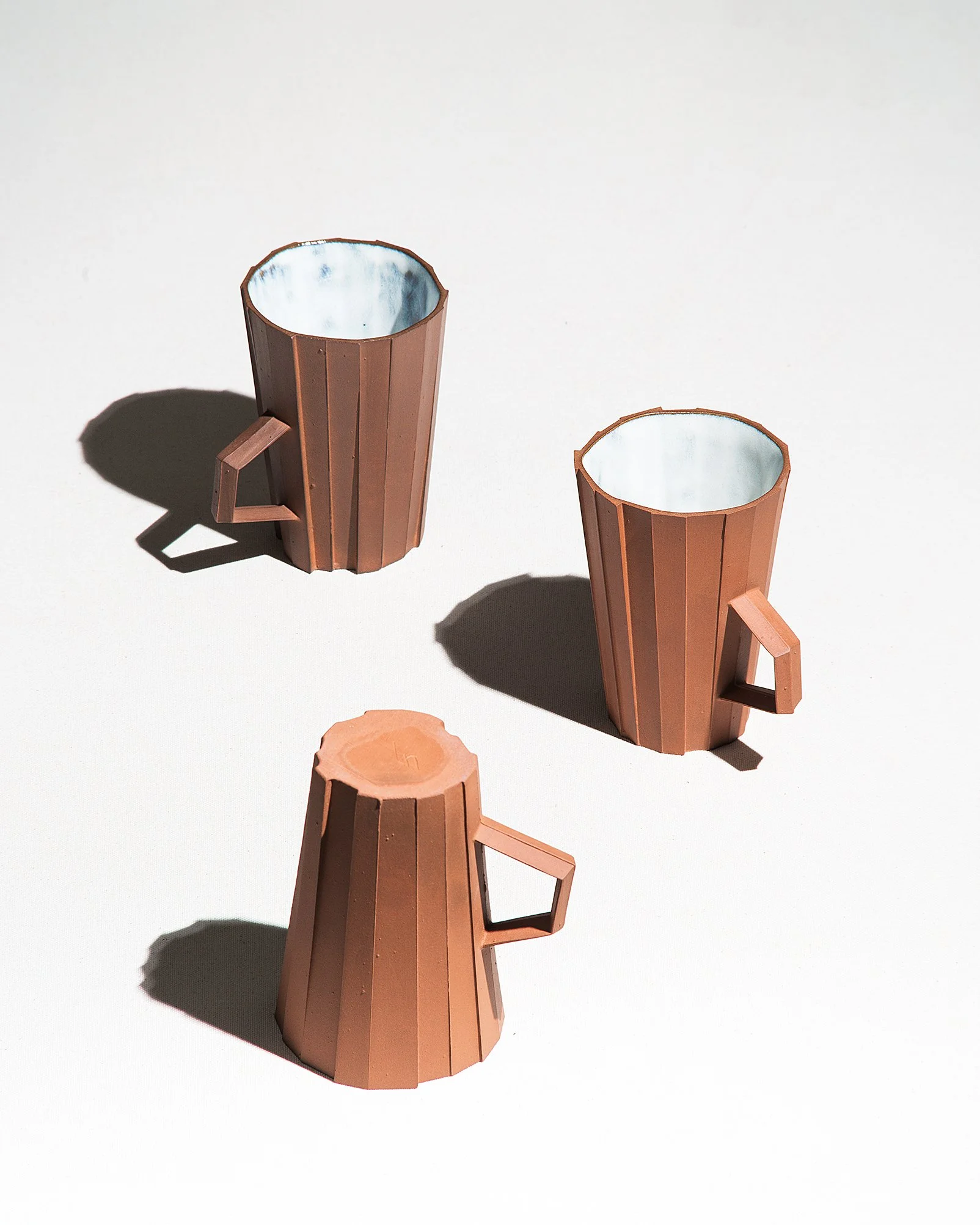 Handmade faceted ceramic cup with unglazed red stoneware exterior and off-white glazed interior, by Lea & Nicolas