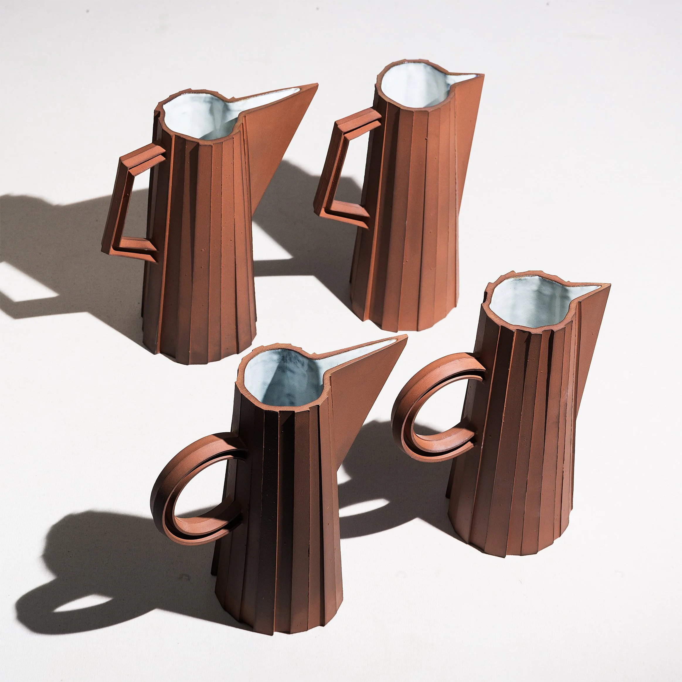 Handmade faceted ceramic pitcher with unglazed red stoneware exterior and off-white glazed interior, by Lea & Nicolas