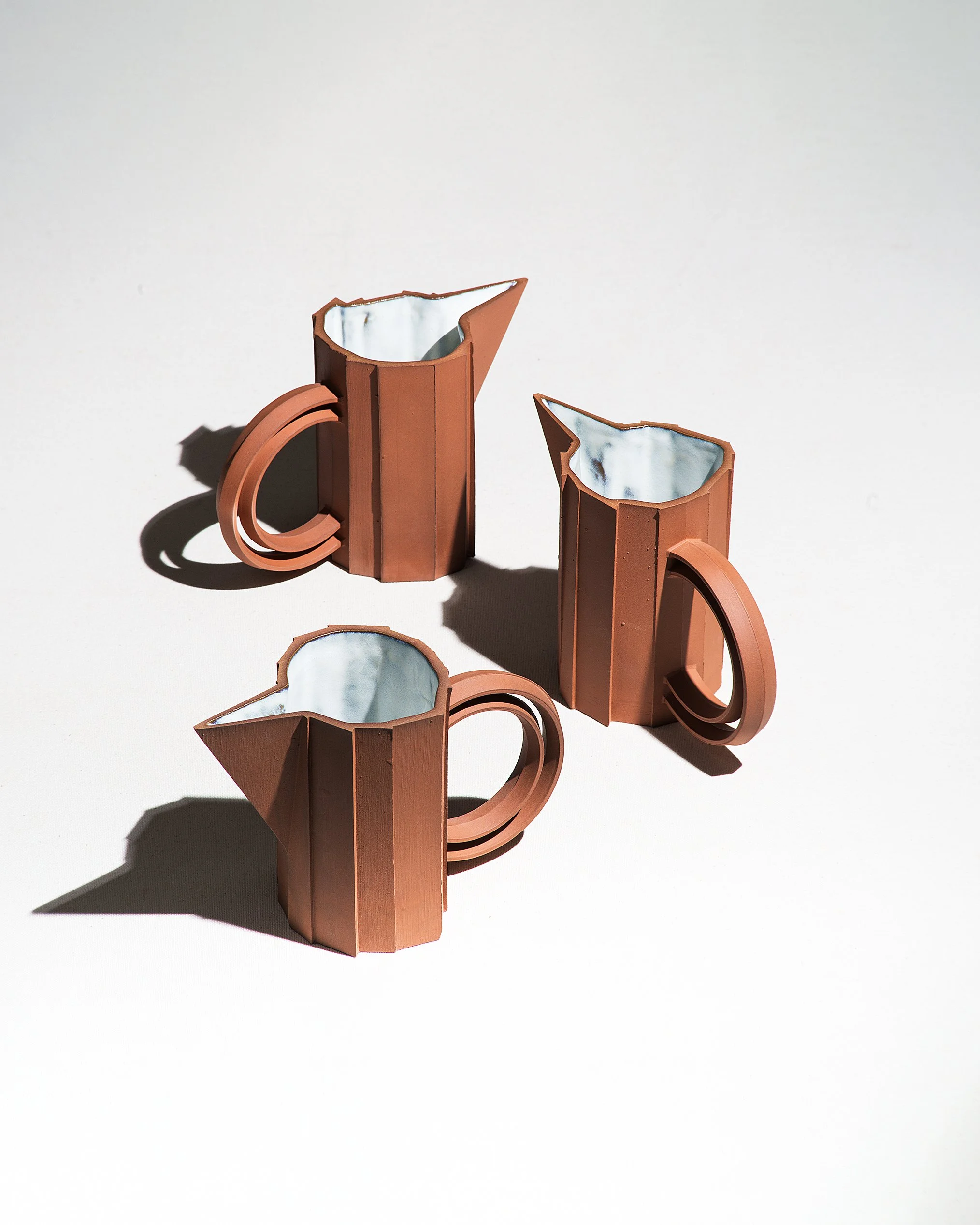 Handmade faceted ceramic pitcher with unglazed red stoneware exterior and off-white glazed interior, by Lea & Nicolas