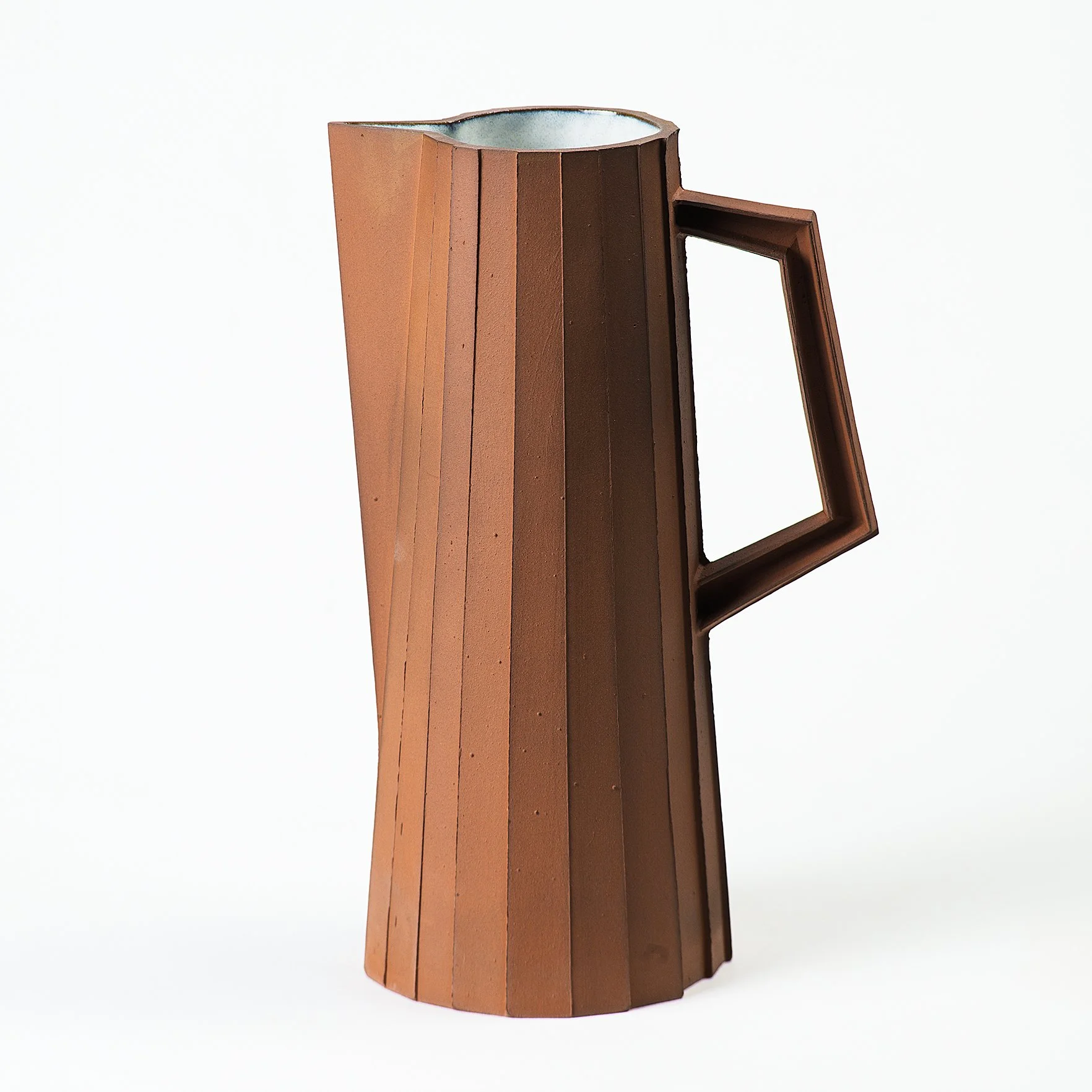 Handmade faceted ceramic pitcher with unglazed red stoneware exterior and off-white glazed interior, by Lea & Nicolas