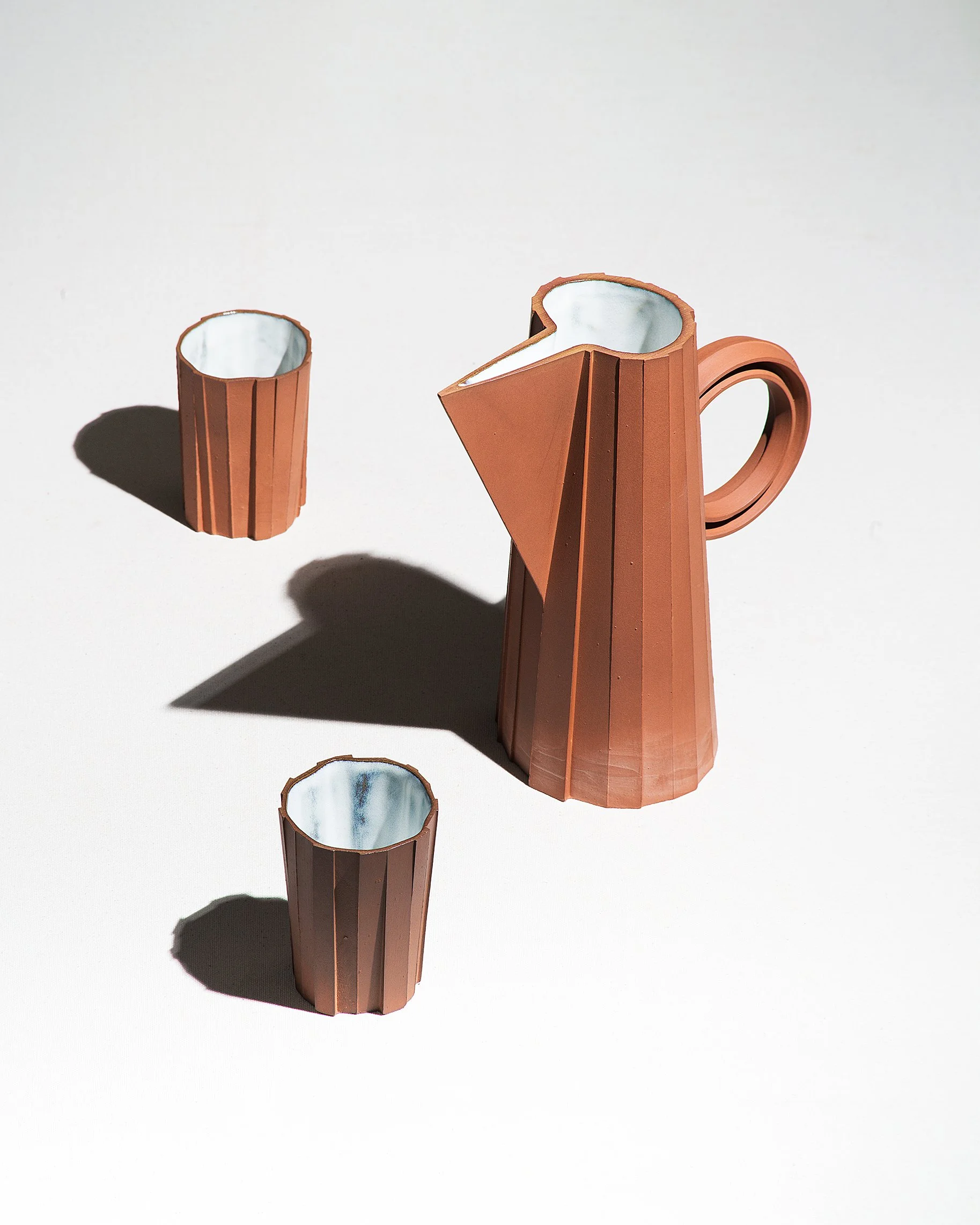 Brutalist handmade ceramic pitcher and tumblers, unglazed red stoneware exterior and off-white glazed interior, by Lea & Nicolas