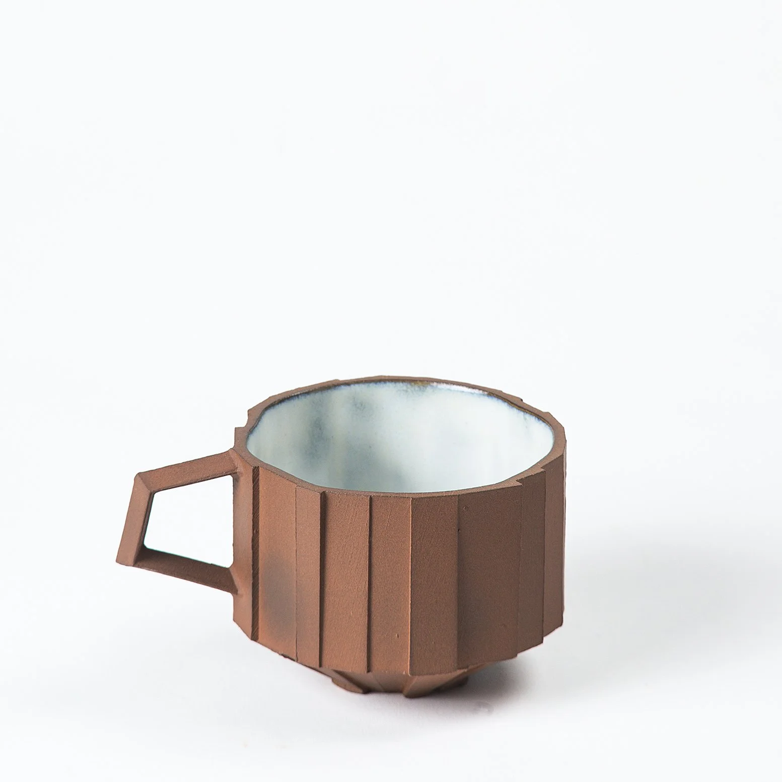 Brutalist handmade faceted ceramic cup with unglazed red stoneware exterior and off-white glazed interior, by Lea Nicolas