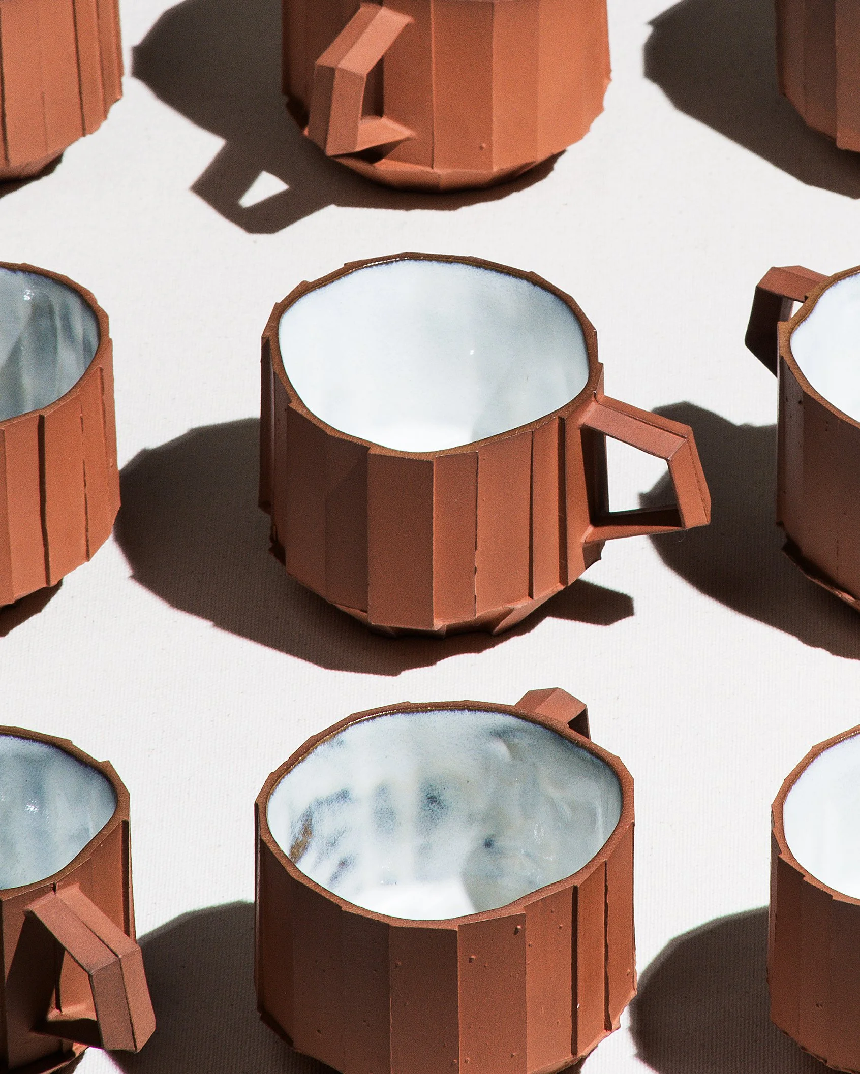 Handmade faceted ceramic cup with unglazed red stoneware exterior and off-white glazed interior, by Lea & Nicolas