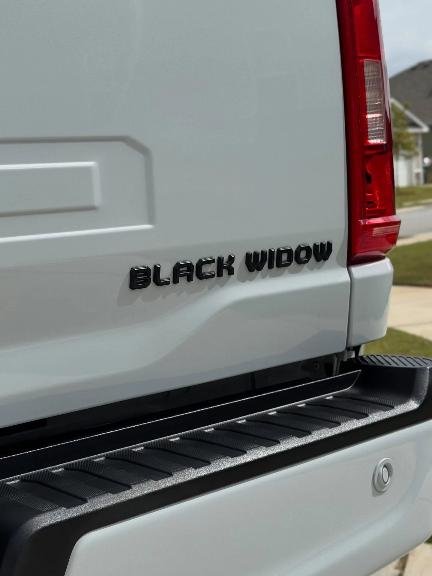 Close-up of a white truck's rear end showing a black emblem that reads 'Black Widow' and part of a red tail light.