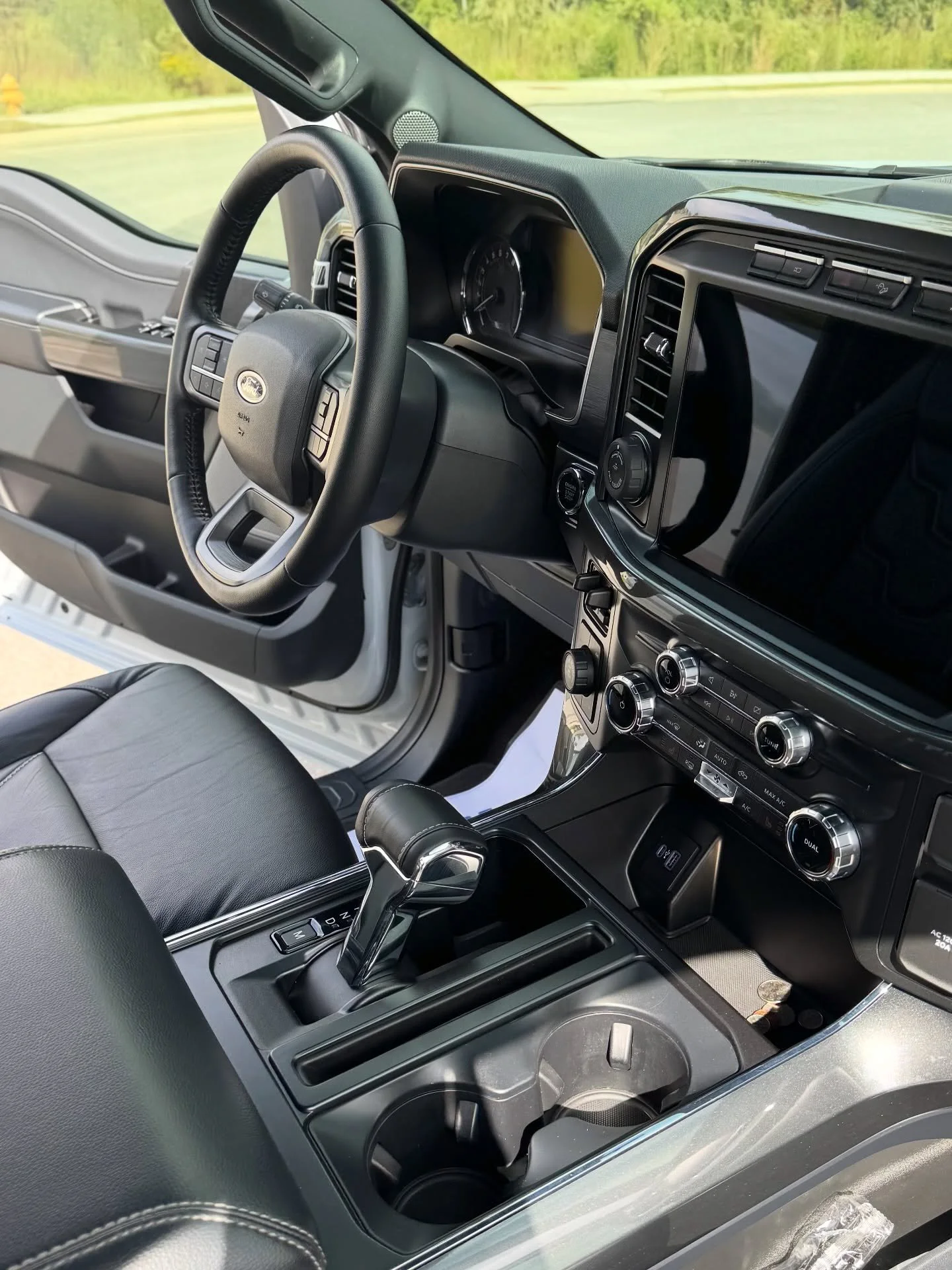 Interior of a modern vehicle showing the steering wheel, dashboard, center console with gear shifter, and cup holders.