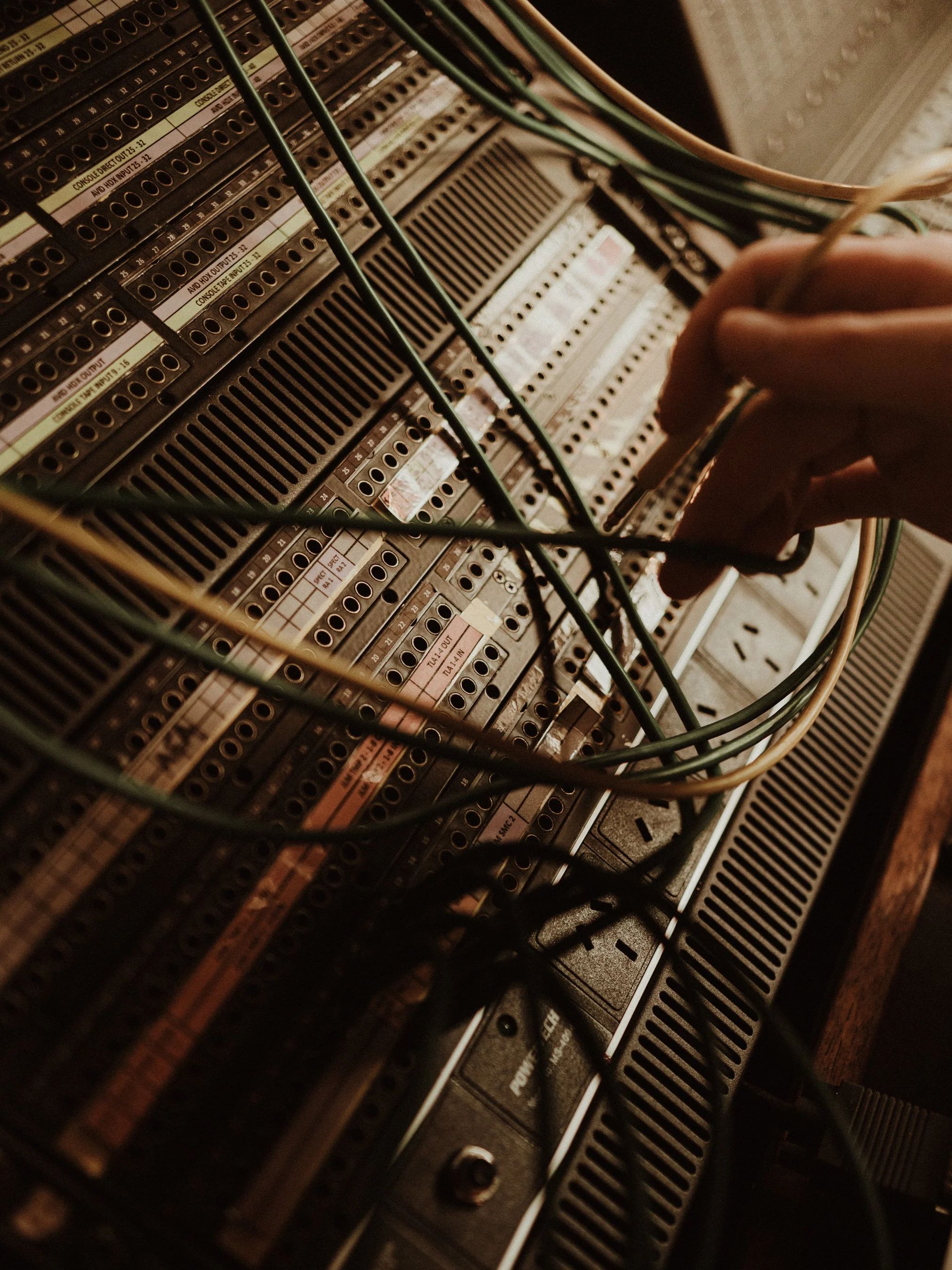Close-up of a person's hand working on a vintage relay panel with multiple wiring connections.