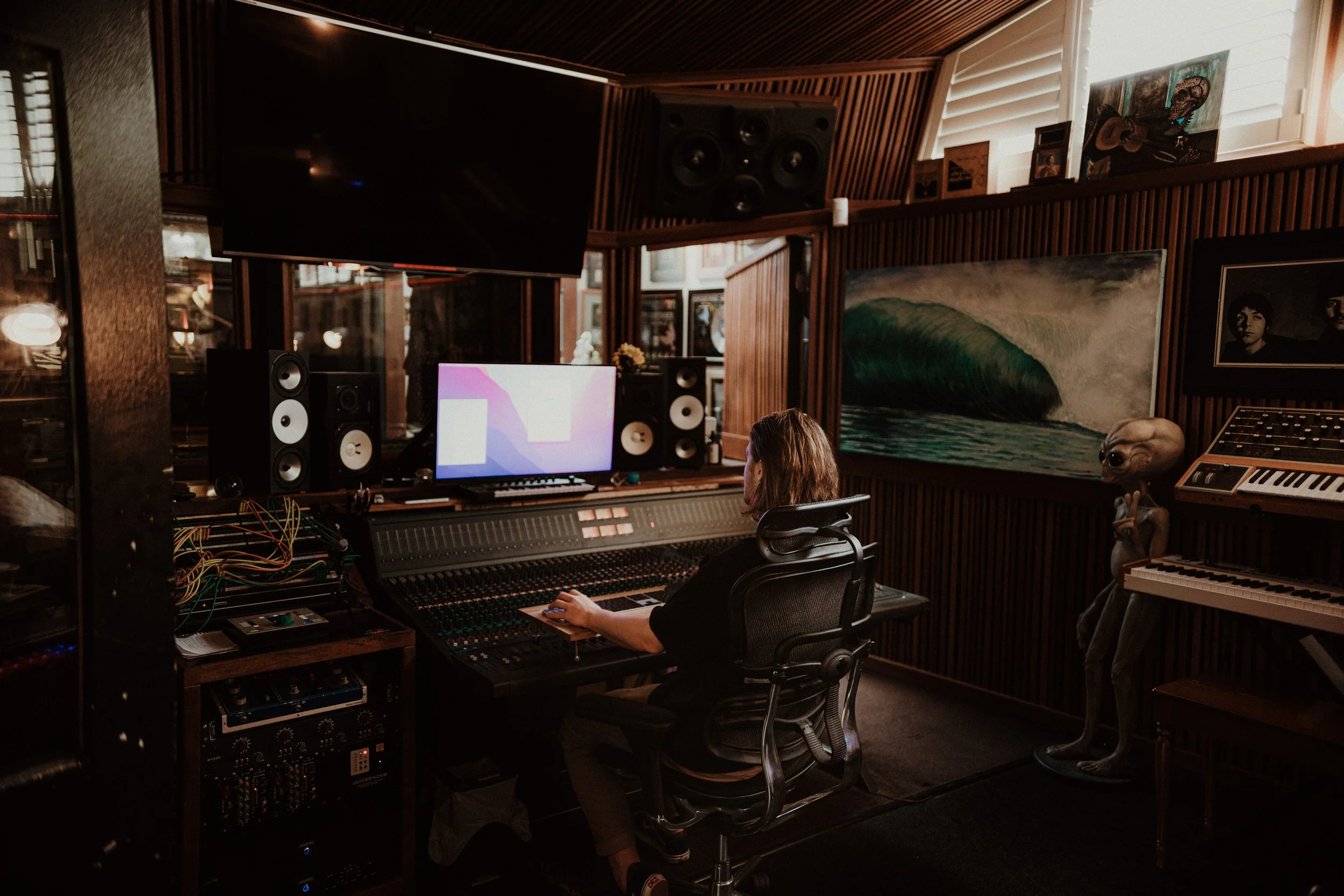 A person working on a music mixing console in a recording studio, surrounded by speakers, artwork, and musical equipment.