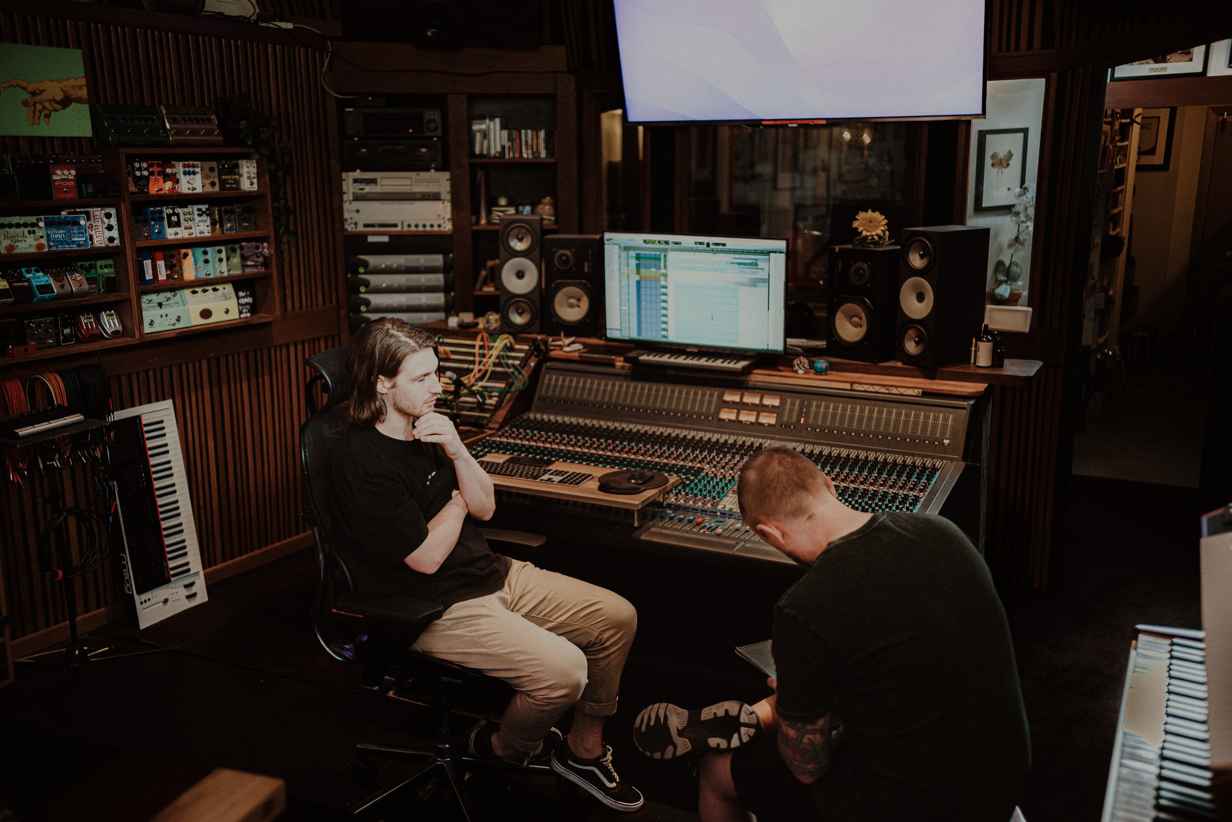 Two men working in a professional recording studio with sound mixing equipment, monitors, and musical instruments.