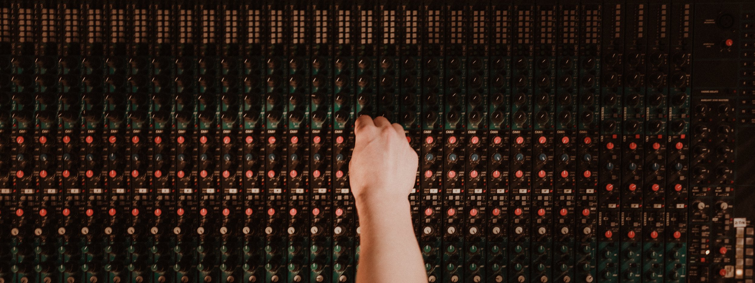A person's hand adjusting knobs on a large audio mixing console with numerous channels.