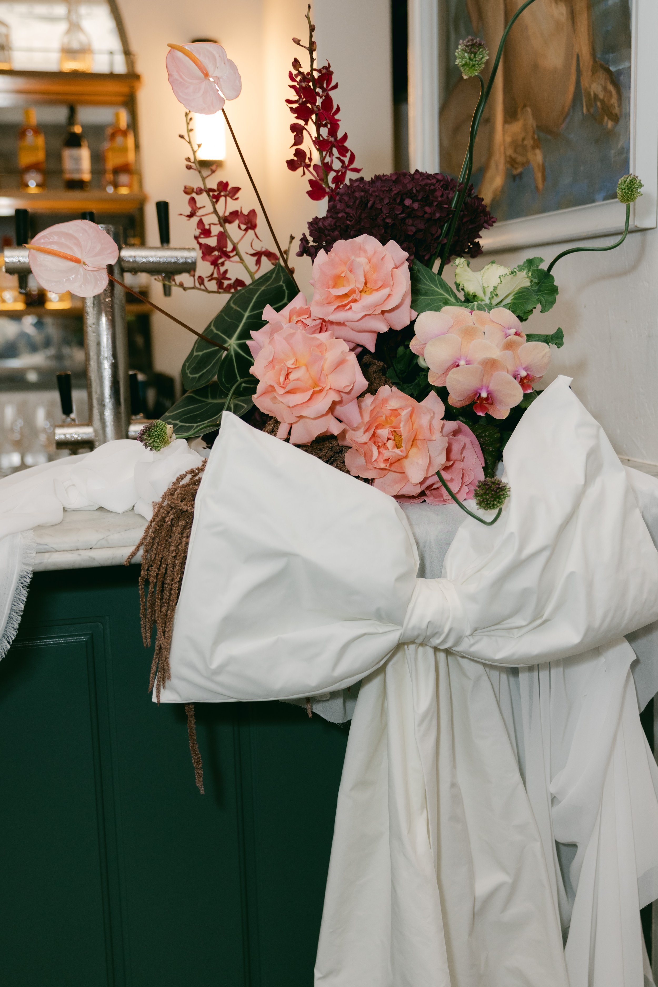 Decorative floral arrangement with pink and purple flowers tied with a large white satin bow.
