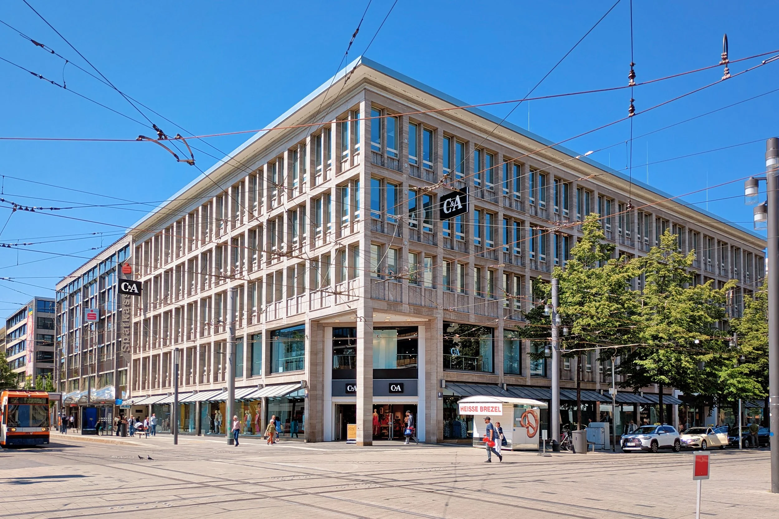 Modernes Wohn- und Geschäftshaus mit Wohnungen in den oberen Etagen und Gewerbeflächen im Erdgeschoss. Das Gebäude steht an einer innerstädtischen Straßenecke und vereint Wohnen und Arbeiten an einem Standort.