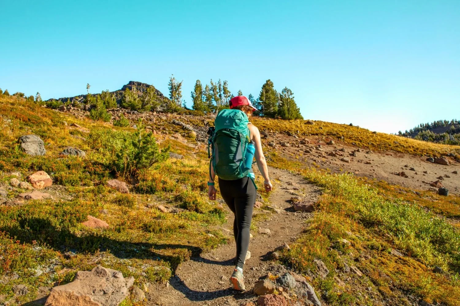 Hornhaut entfernen - Frau mit Rucksack und sommerlichem Outfit wandert einem Berggrat entgegen.