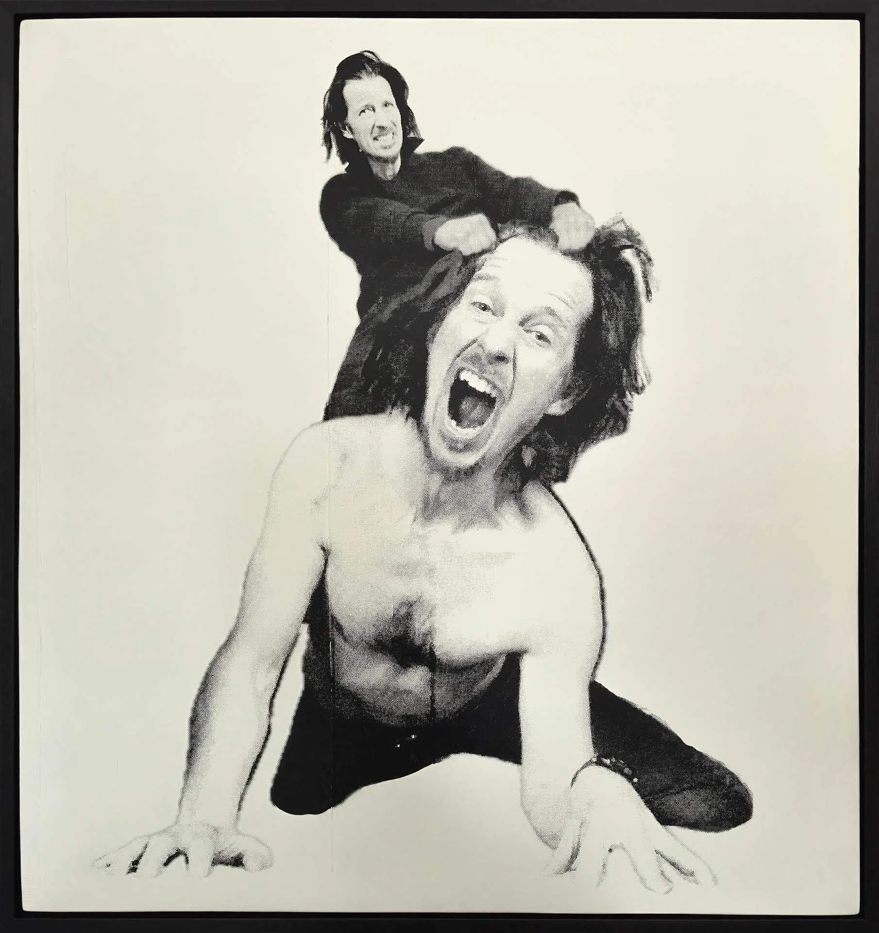 Black and white photo of a person with long hair kneeling on the floor with an open mouth, and another person with short hair standing behind him, pulling his hair.
