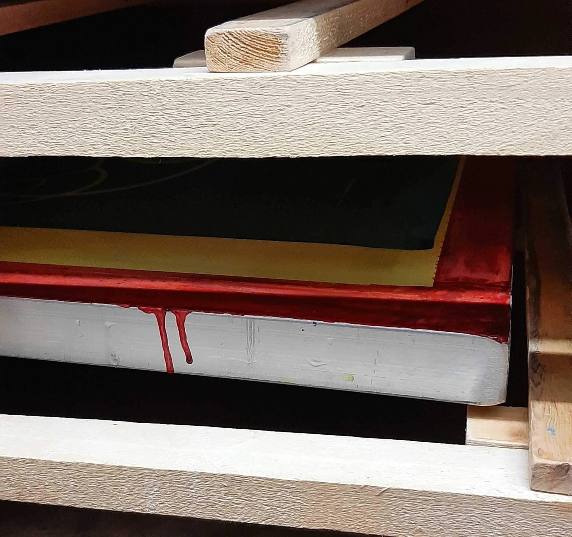 Screen printing frames stacked inside a wooden drying cupboard, showing emulsion‑coated mesh and red ink residue.