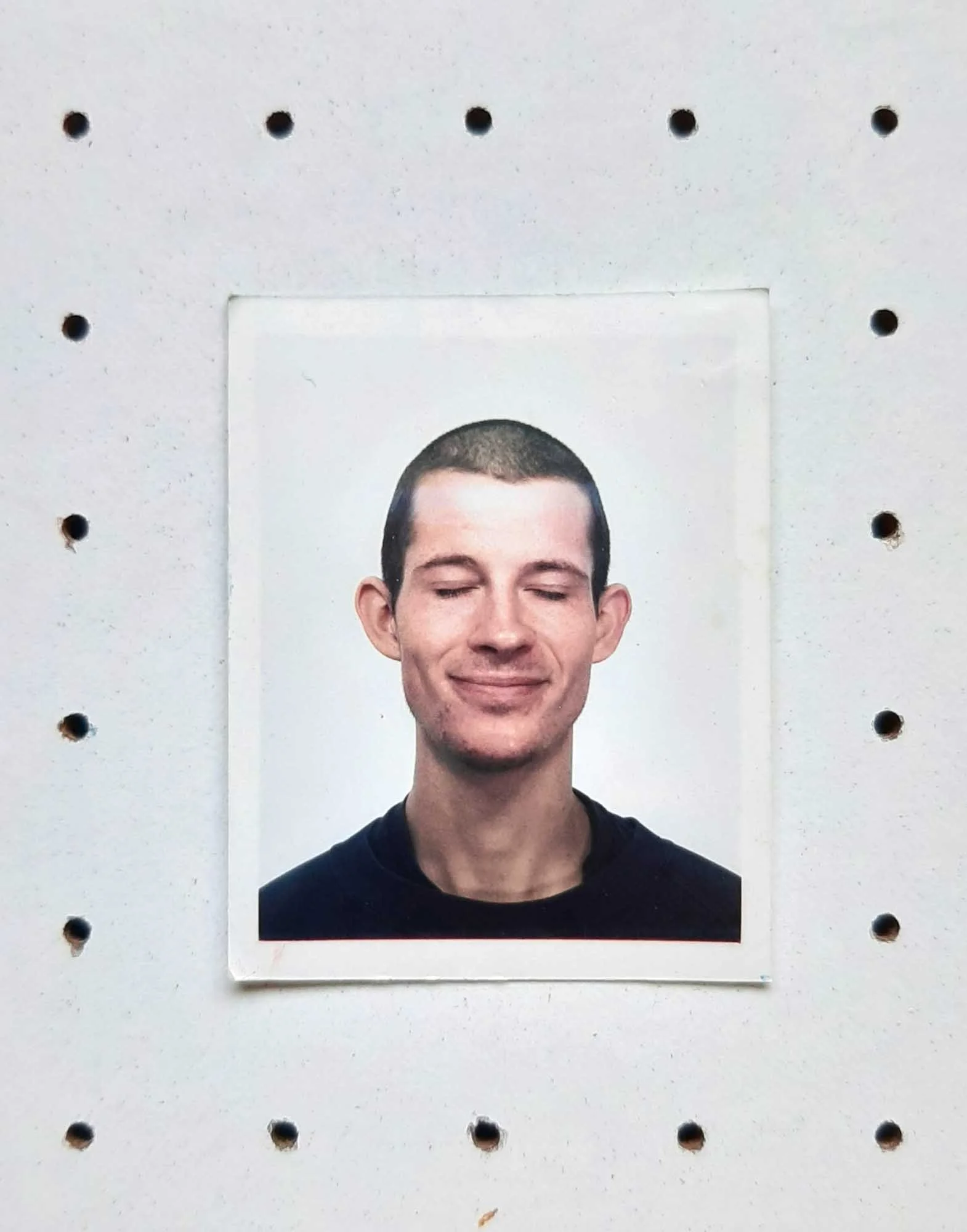 Photograph of a young man with short hair and a faint smile, with closed eyes, against a plain white background.