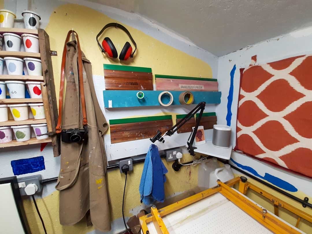 Wall‑mounted squeegees, ink shelf, apron and vacuum table setup in a compact screen printing workspace.