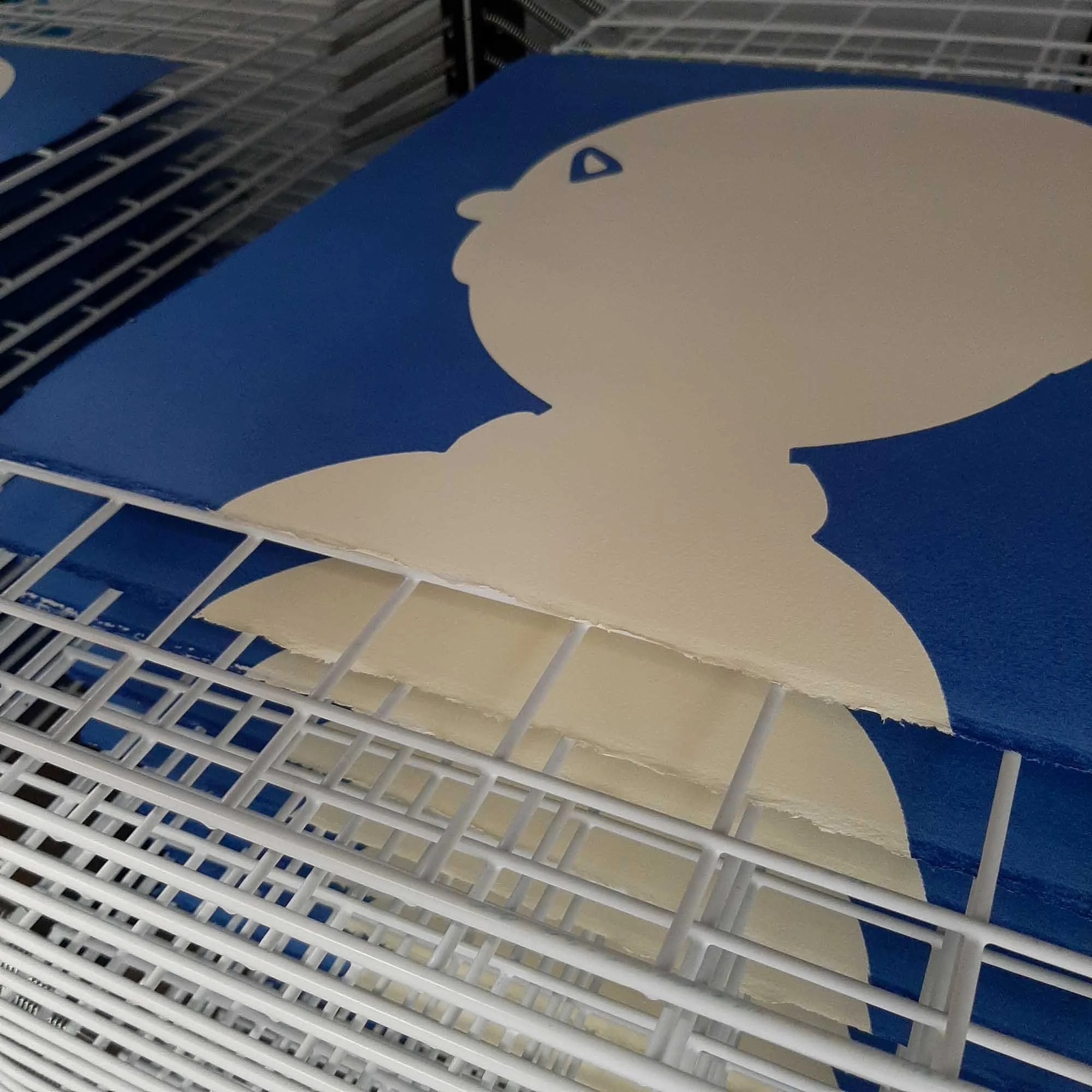 Stack of screen prints drying on a wire rack, showing repeated cream silhouettes on blue backgrounds.