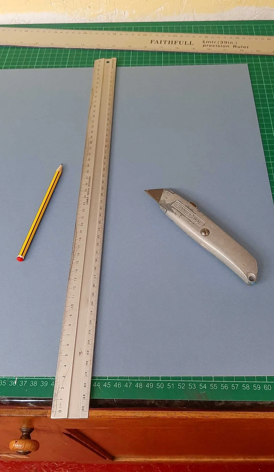 Metal rulers and utility knife placed on a cutting mat, used for measuring and trimming in screen printing.