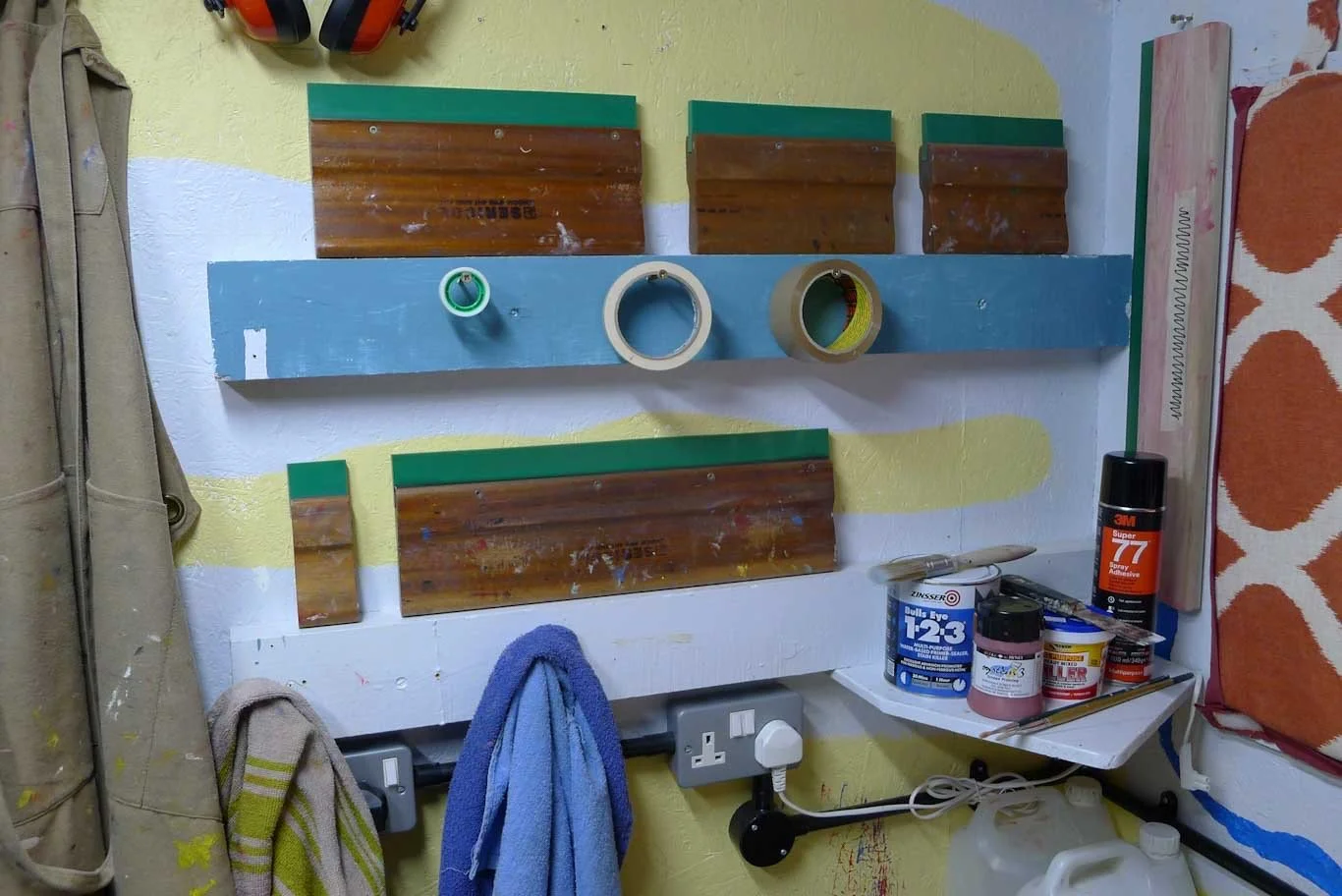 Wooden and aluminium squeegees of different lengths stored on a shelf in a printmaking studio