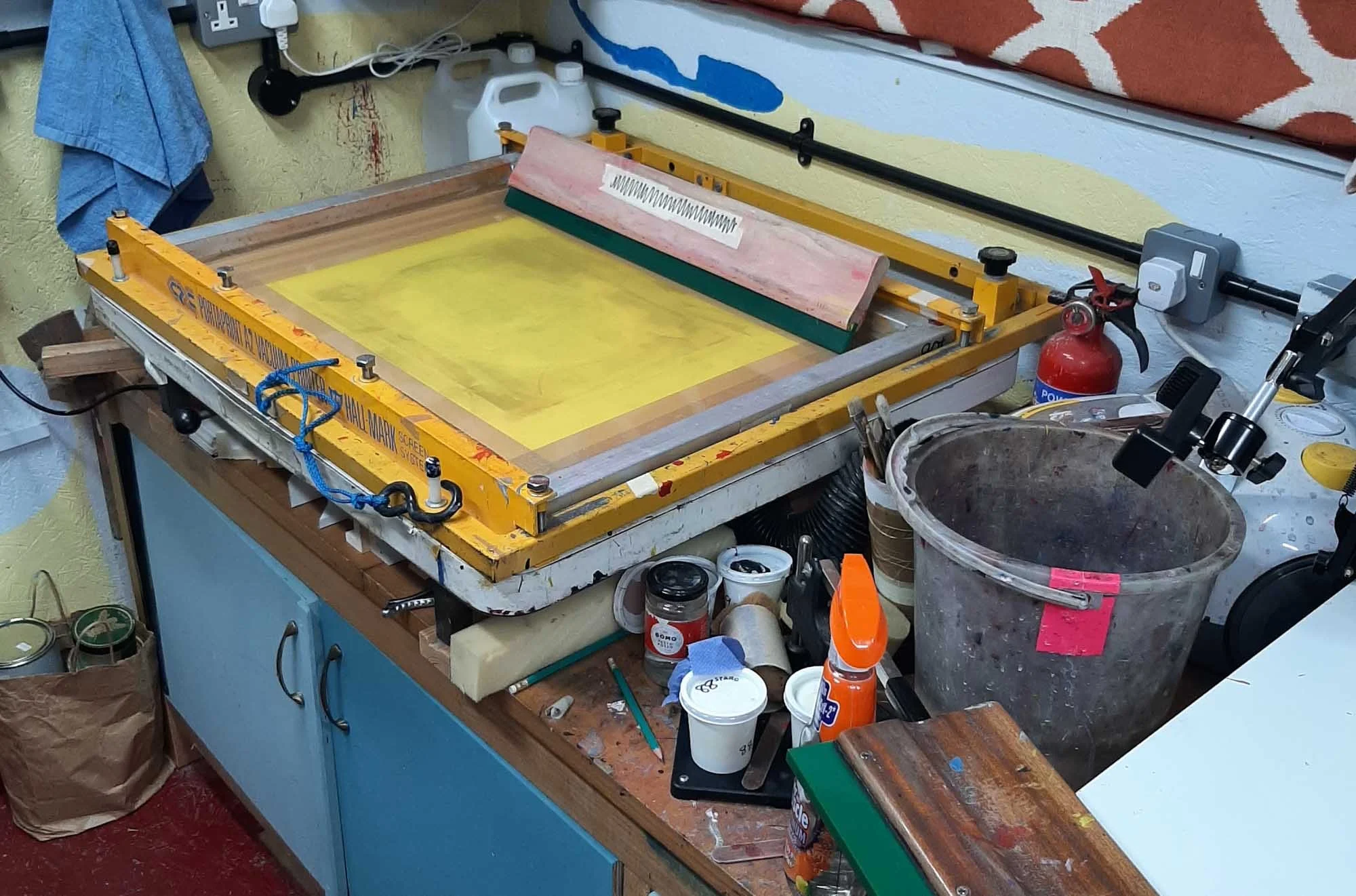 Silkscreen frame clamped onto press bed with registration sheet for alignment.